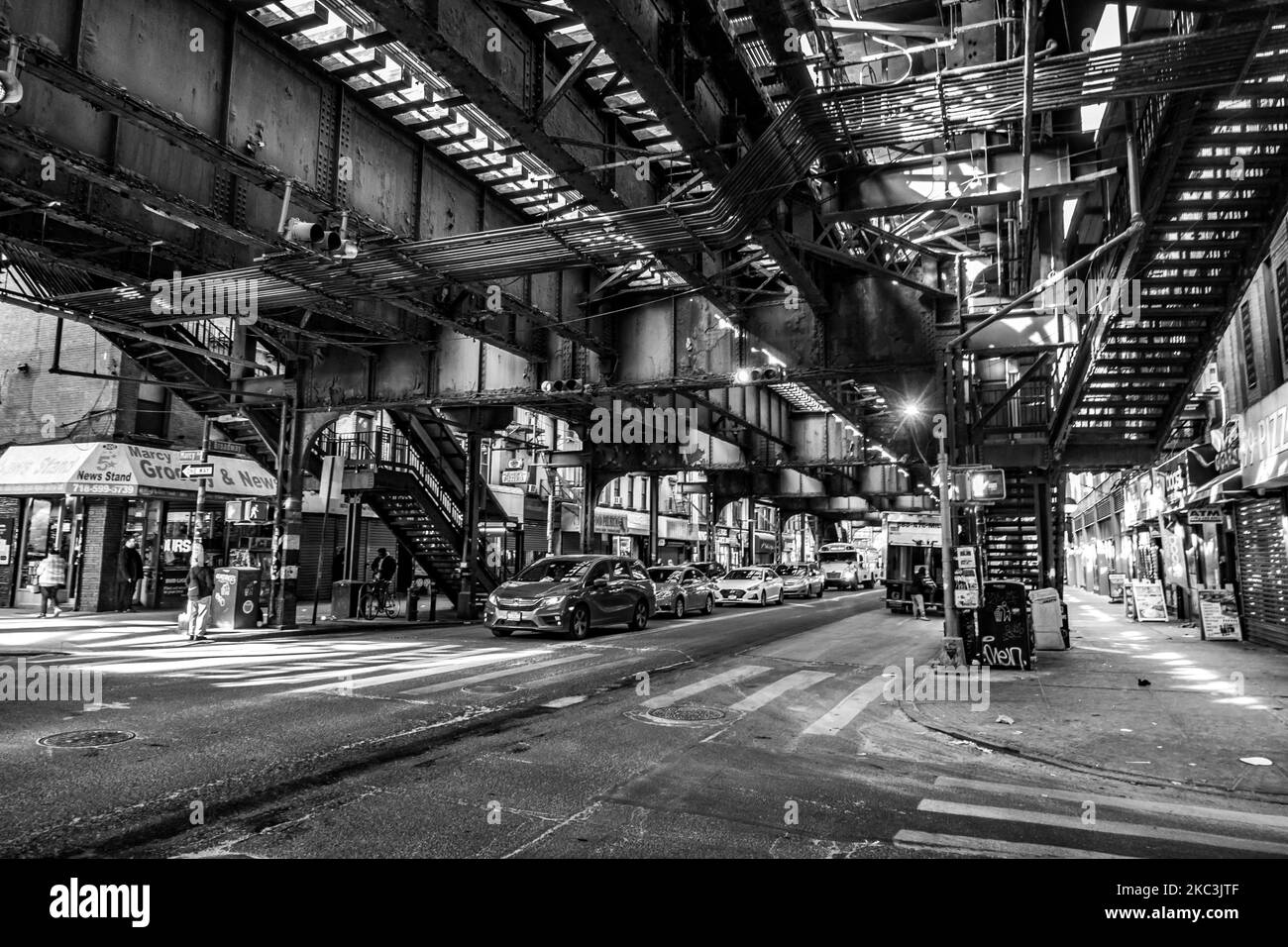 (EDITOR'S NOTE: Image was converted to black and white) Daily life view of the road and street under the subway railroad air-bridge metal construction of M, J and Z lines near Marcy Ave station, with restaurants, shops, the famous dollar slice pizza, traffic with cars and trucks and with sidewalks in Broadway street in Brooklyn, New York City. Brooklyn is the most populous county in the state of New York and the second-most densely populated in the United States. Brooklyn, NY, USA on 13 February 2020. (Photo by Nicolas Economou/NurPhoto) Stock Photo