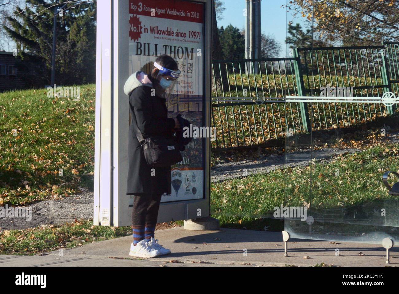 Woman wearing a plastic face shield and face mask as she waits for a public bus during the novel coronavirus (COVID-19) pandemic in Toronto, Ontario, Canada on November 12, 2020. Ontario reported 1,575 new COVID-19 cases today and 18 more deaths, setting a new single-day record for daily cases reported in a 24-hour period since the start of the pandemic. New modeling projections warn that Ontario could see 6,500 daily cases of COVID-19 by mid-December. The projections also suggest that the number of COVID-19 patients in intensive care units will exceed the 150 threshold within two weeks, overw Stock Photo