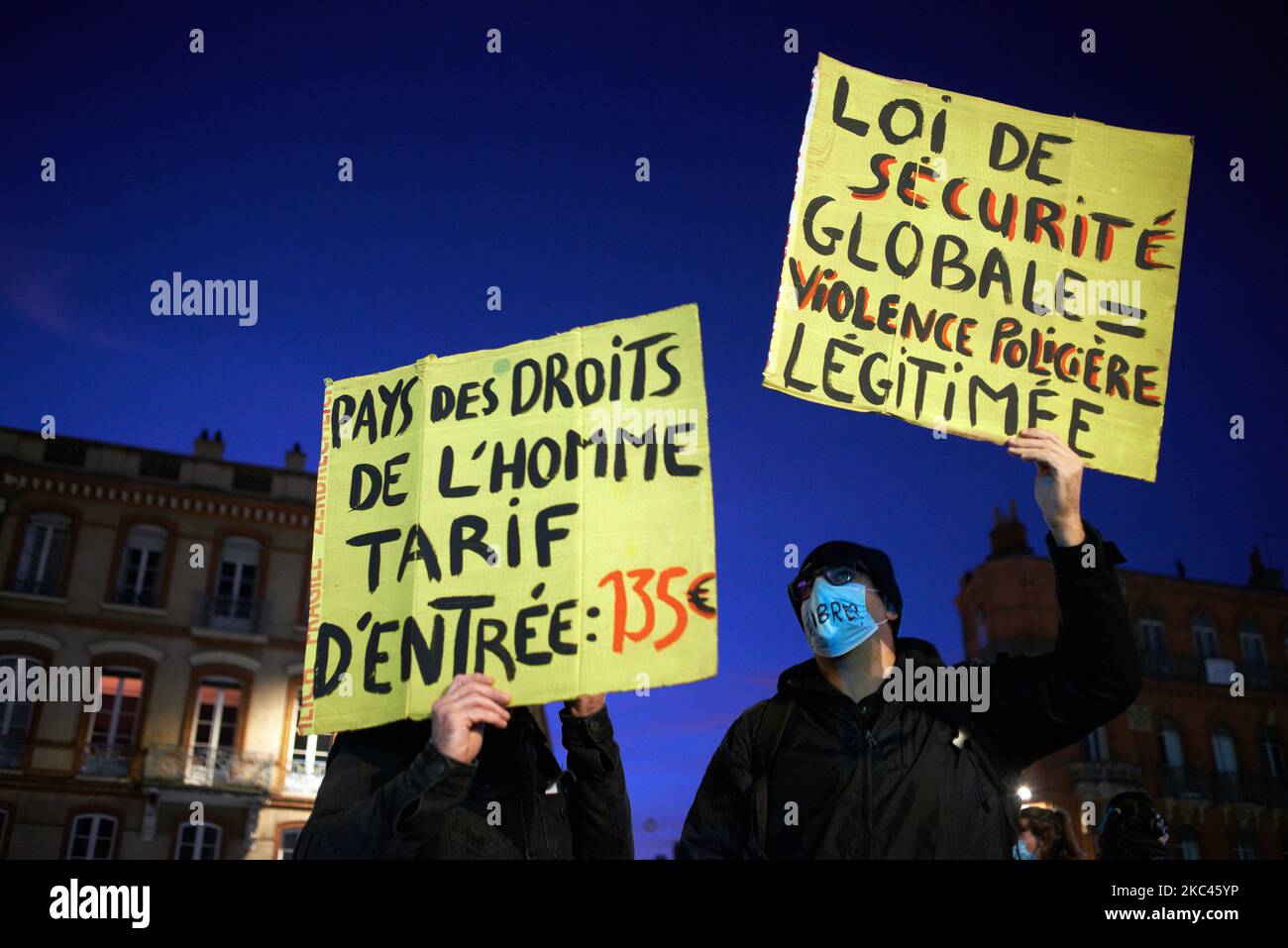 Two protesters hold placards reading (left) 'Human Rights Country: entrance fee €135' and 'Global Security Law= legalized police violence' (right). Several NGOs (Amnesty International, Human Rights League), trade unions (CGT, CNT, CFDT, SAF ie Union of French Lawyers), journalists' unions (SNJ, SNJ-CGT), International and European Journalists Federation, and political parties called for a gathering against the so-called 'Global Security Law' bill promoted by French President Macron and his majority. The gathering finished amid clouds of tear gas launched by riot police. This law intends to giv Stock Photo