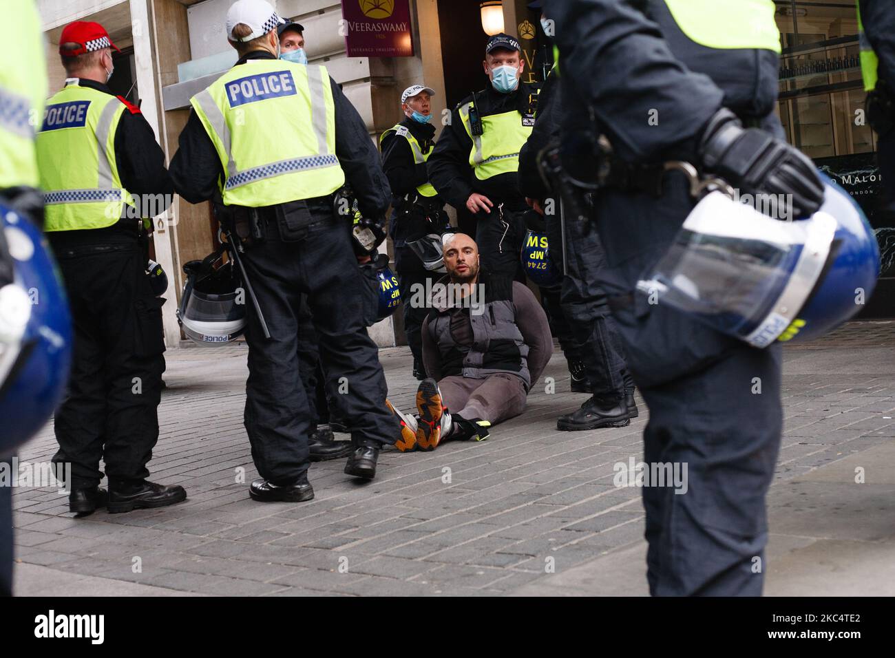 An arrested anti-lockdown activist waits to be transported away following scuffles with police officers on Regent Street in London, England, on November 28, 2020. In an evening update the Metropolitan Police announced it had made 155 arrests over the course of the day's demonstrations, for offences including breaches of coronavirus regulations, assault on police and possession of drugs. London is to return to 'Tier 2' or 'high alert' covid-19 restrictions once the current England-wide coronavirus lockdown ends next Wednesday. All three of the tiers, assigned to local authorities across England Stock Photo