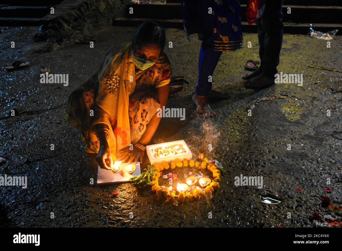 A lady wearing mask decorates a river bank with earthen lamps on the