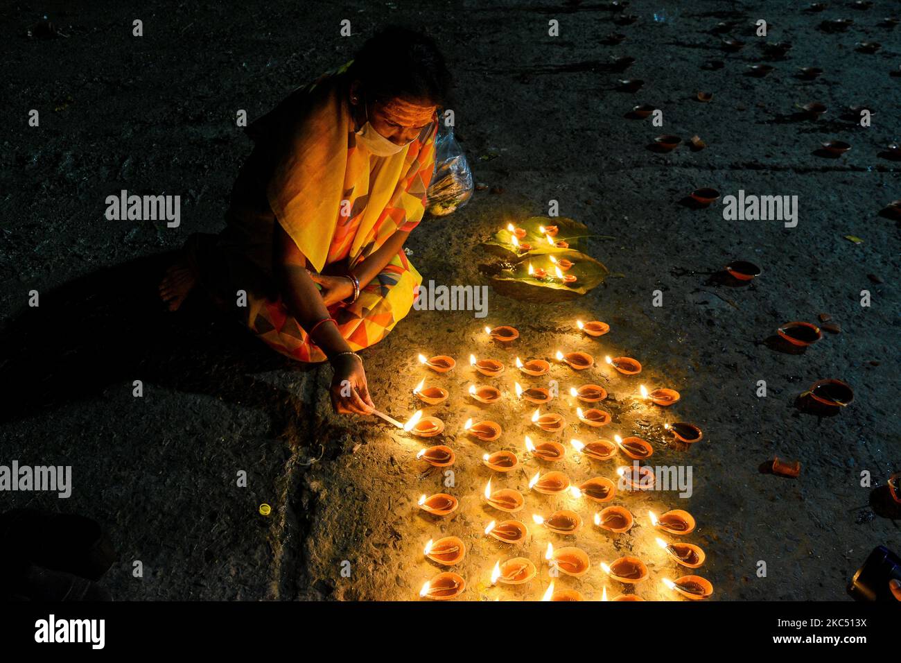 A lady wearing mask lights oil lamp on the day of Dev Deepawali at a