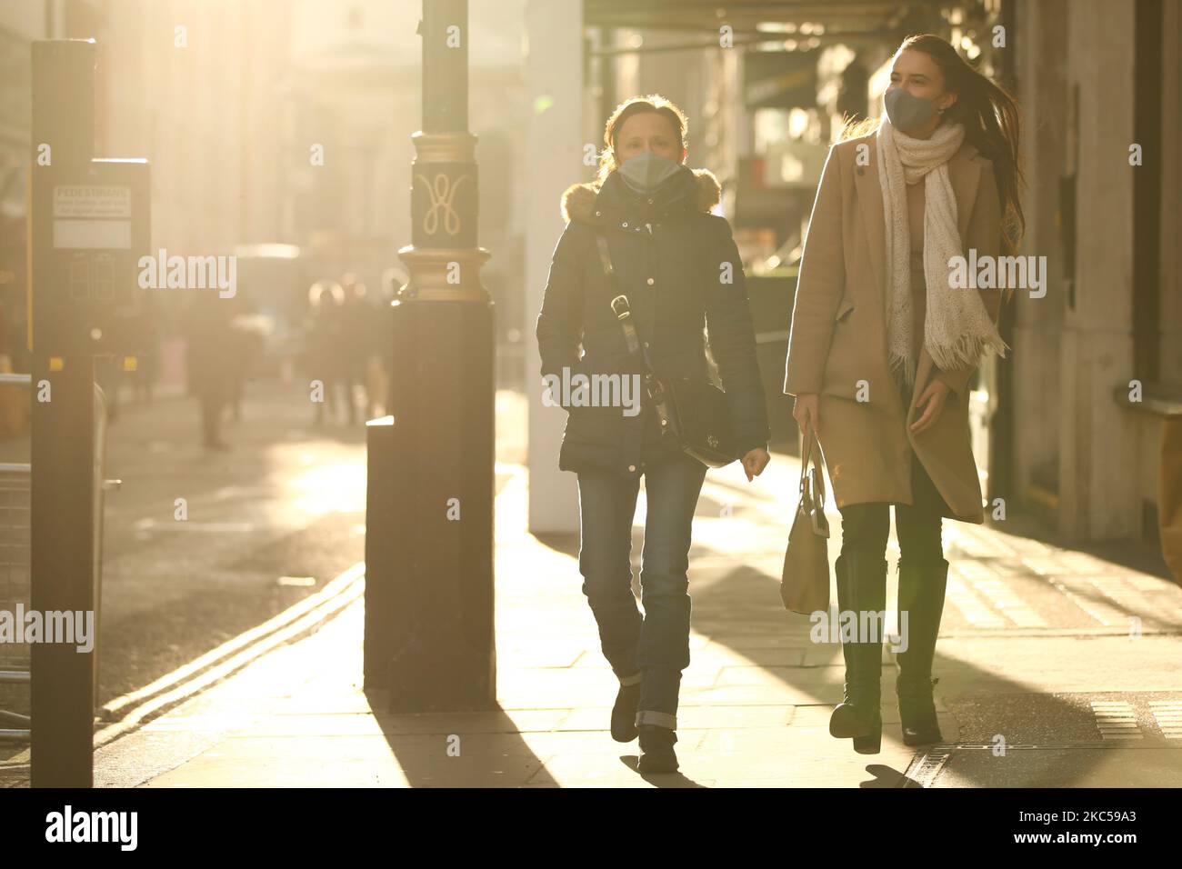 Women wearing face masks walk in winter sunlight on Maddox Street in London, England, on December 5, 2020. London has returned to so-called Tier 2 or 'high alert' coronavirus restrictions since the end of the four-week, England-wide lockdown last Wednesday, meaning a reopening of non-essential shops and hospitality businesses as the festive season gets underway. Rules under all three of England's tiers have been strengthened from before the November lockdown, however, with pubs and restaurants most severely impacted. In London's West End, meanwhile, Oxford Street and Regent Street were both pa Stock Photo