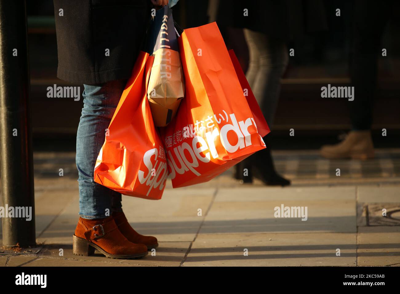 A shopper stands with bags from clothing retailers Superdry and Hollister on Maddox Street in London, England, on December 5, 2020. London has returned to so-called Tier 2 or 'high alert' coronavirus restrictions since the end of the four-week, England-wide lockdown last Wednesday, meaning a reopening of non-essential shops and hospitality businesses as the festive season gets underway. Rules under all three of England's tiers have been strengthened from before the November lockdown, however, with pubs and restaurants most severely impacted. In London's West End, meanwhile, Oxford Street and R Stock Photo