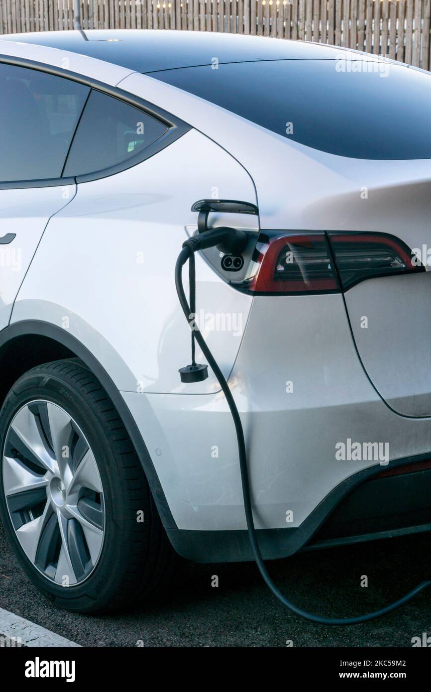 A white Tesla electric car charging at a public recharging point. Stock Photo