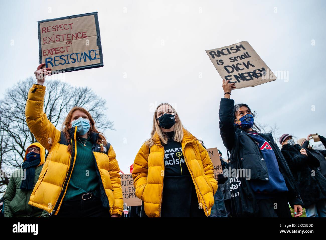 Three women are holding placards and wearing t shirts against racism 