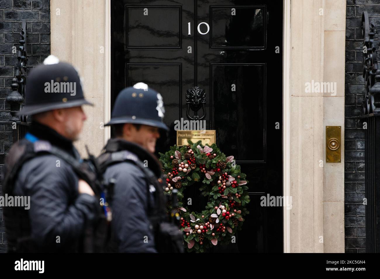 Police officers walk past the door of 10 Downing Street, adorned with a Christmas wreath for the festive season, in London, England, on December 9, 2020. (Photo by David Cliff/NurPhoto) Stock Photo