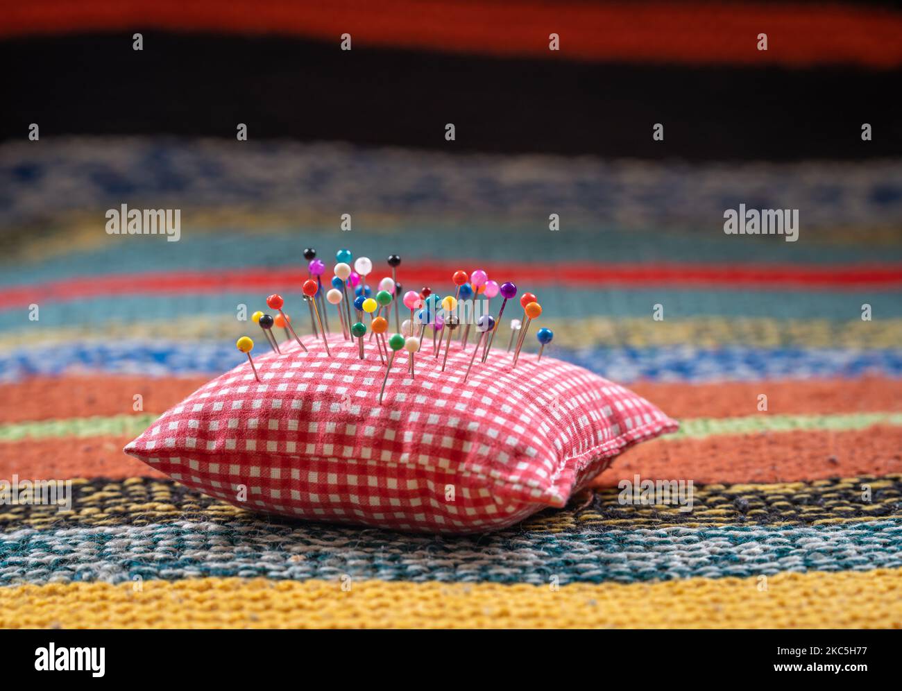 Pin cushion with colorful pinheads on soft and warm knitted background, selective focus Stock Photo