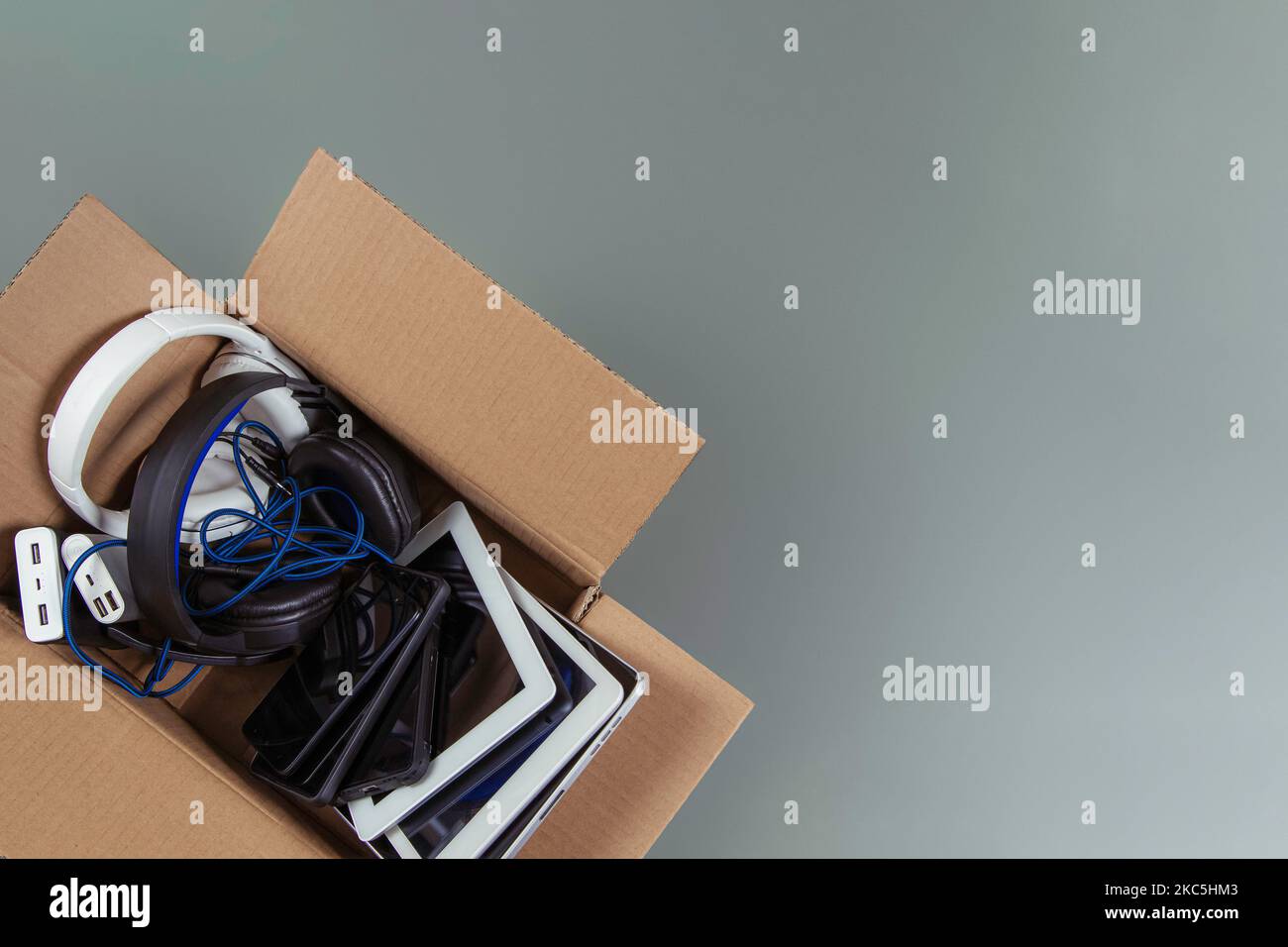 Cardboard box full of old used computers, digital tablets, smartphones, electronic gadgets for recycling on gray background. Donation, e-waste Stock Photo