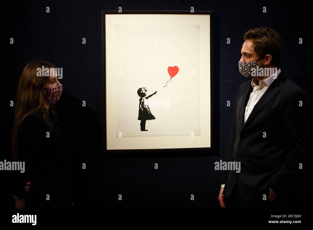 Members of staff wearing face masks pose with 'Girl with Balloon', by British artist Banksy, estimated at 120,000-180,000GBP, during a photo call for the upcoming Prints and Multiples sale at Bonhams auction house in London, England, on December 10, 2020. The sale takes place next Tuesday, December 15. (Photo by David Cliff/NurPhoto) Stock Photo
