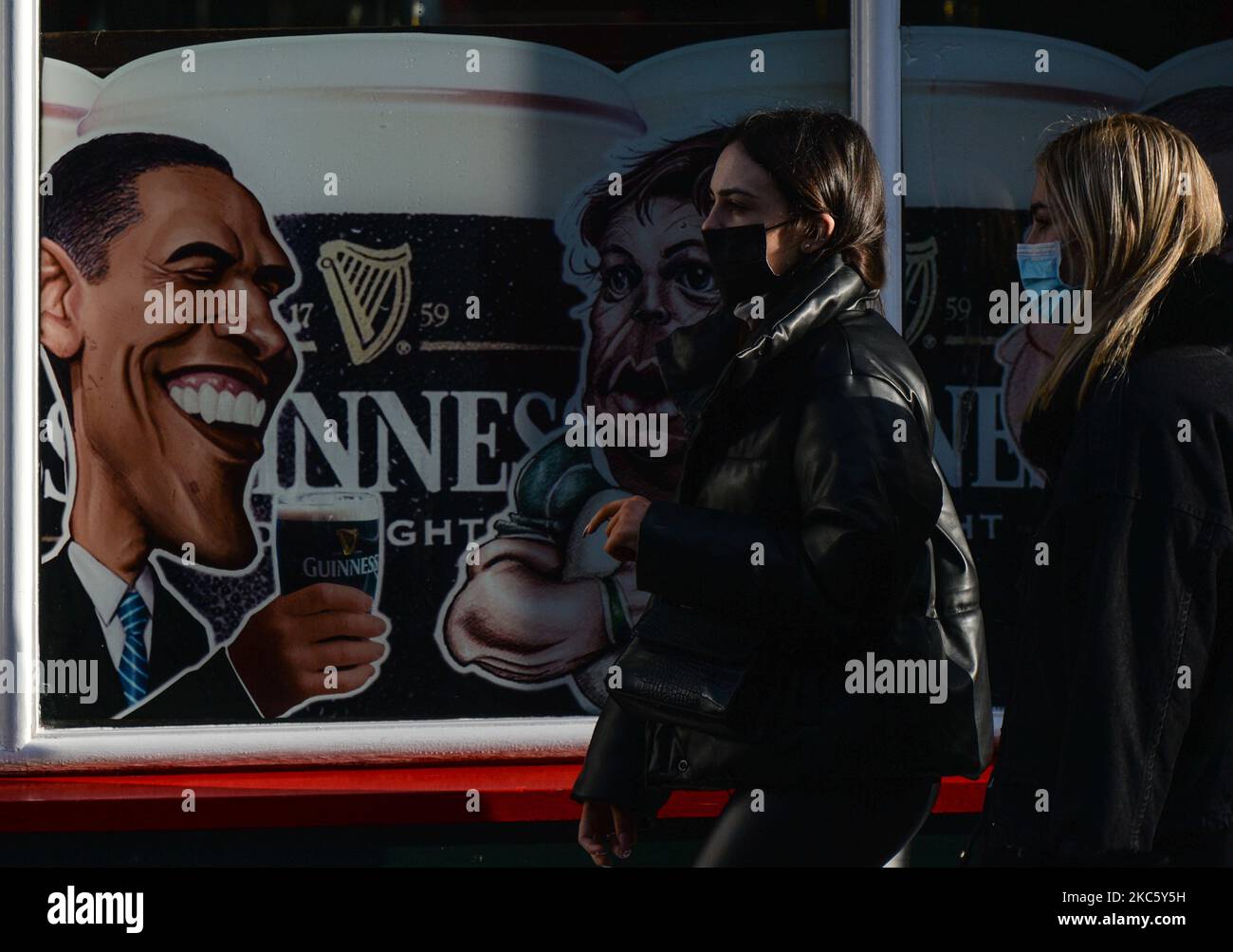 Two young women wearing face masks, walk by an image of a former U.S. President Barack Obama seen on a pub facade in Dublin's city center. On Tuesday, December 15, 2020, in Dublin, Ireland. (Photo by Artur Widak/NurPhoto) Stock Photo
