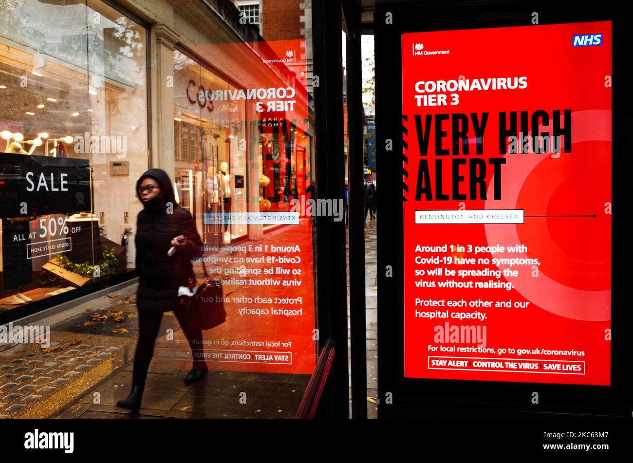 A woman walks past a notice for 'Tier 3' or 'Very High' alert