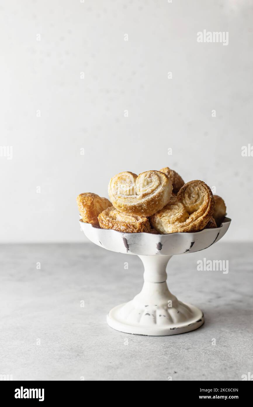 Puff pastry cookies palmier or elephant ears, crunchy pastry heart shaped in white dish on gray background isolated Stock Photo