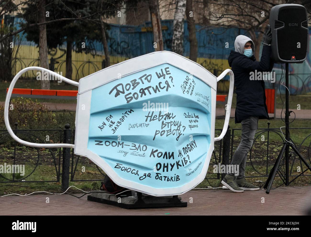 A man wearing a protective face mask amid the COVID-19 coronavirus epidemic stands next to an art-object of the largest medical mask in Ukraine during an event on Kontraktova Square in the center of Kyiv, Ukraine on 28 December 2020. The event named 'Cover yourself with a mask, not inside yourself' is a part of the social campaign aimed to draw attention to mental health problems during the Covid-19 coronavirus pandemic, as local media reported. The mask letterings like: 'If only not to get sick',' I'm afraid for my parents',' Will I really lose my job?','When will I see my grandchildren?', 'H Stock Photo