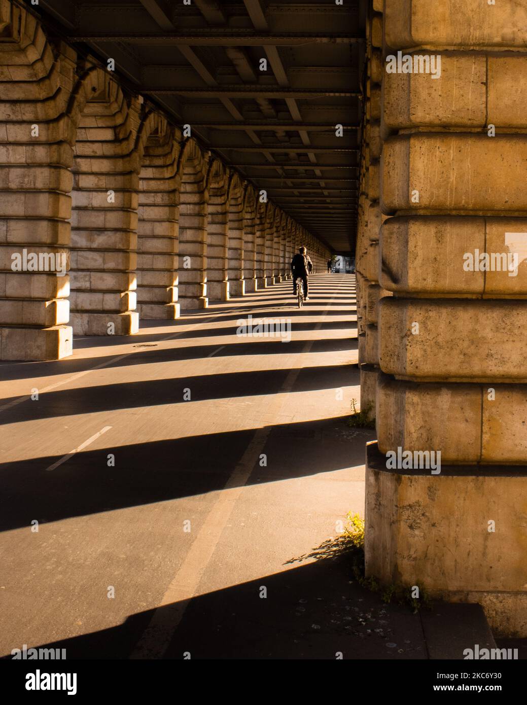 A person cycling under a bridge with columns in Paris in the shadows Stock Photo