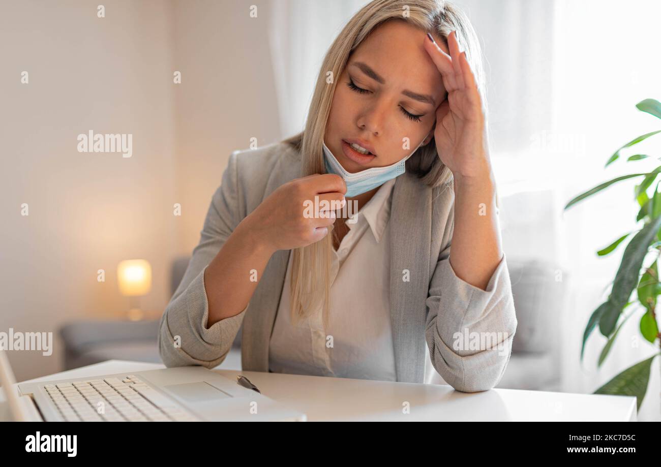 Woman working in the office and having difficulties breathing with face mask, she is pulling the mask down.The woman had to remove the mask to breathe Stock Photo