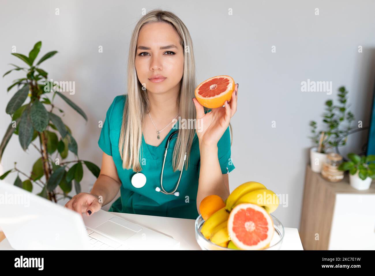 Female nutritionist with fruits working at her desk. Smiling nutritionist in her office, she is showing healthy vegetables and fruits, healthcare Stock Photo