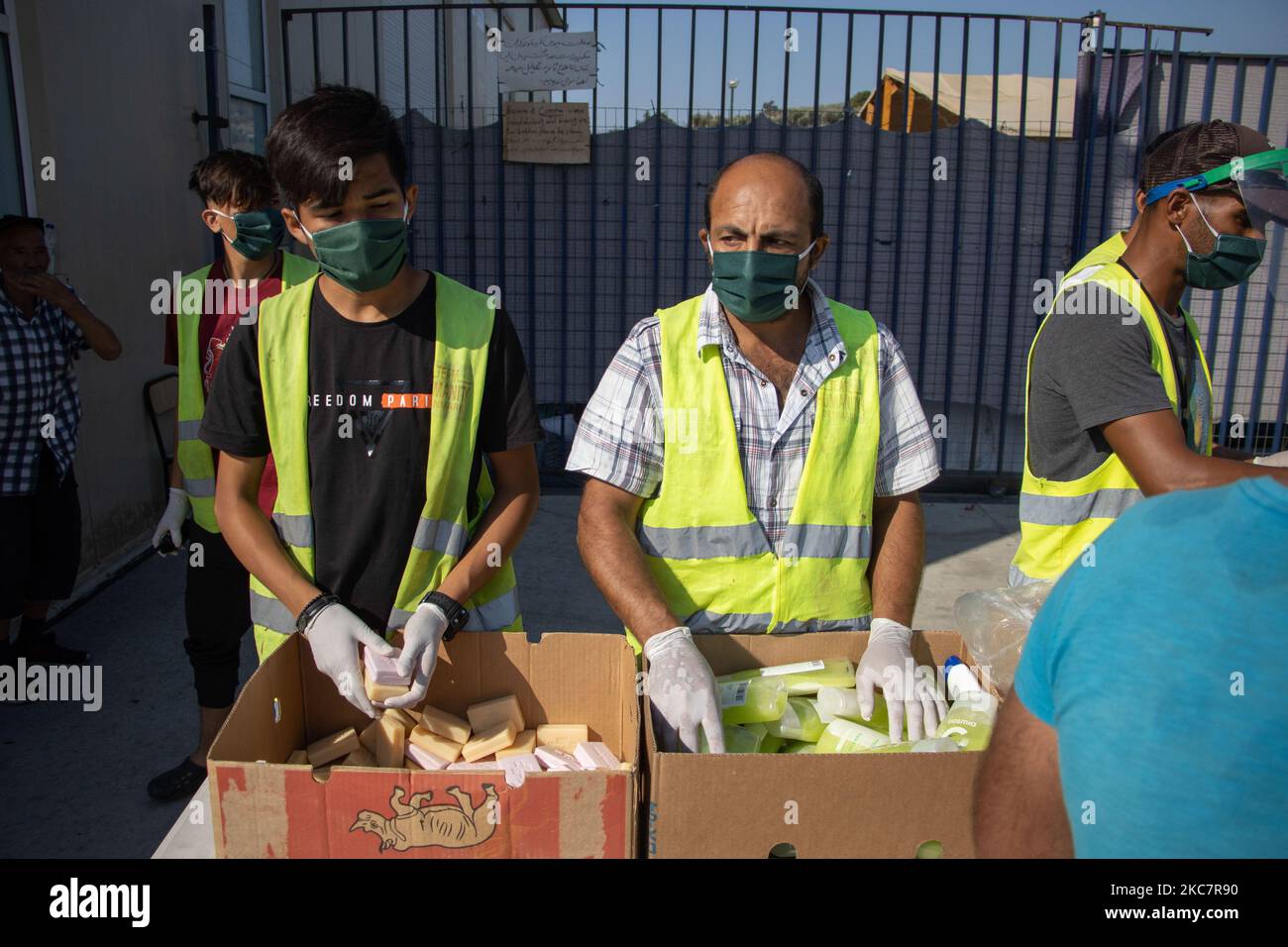 People of the organization and volunteers with all the safety preventive measures like facemask, faceshield and gloves are distirbuting humanitarian Aid to Asylum Seekers from Team Humanity Denmark NGO after the refugees and migrants have their body temperature tested, in order to prevent people to enter the facility with the possibility of spreading the pandemic, the Covid-19 Coronavirus. The facility is near the former Moria hotspot camp. More than 10.000 Asylum Seekers are homeless and helpless, resulting sleeping and living roadside without any shelter, food, running water supply, facility Stock Photo