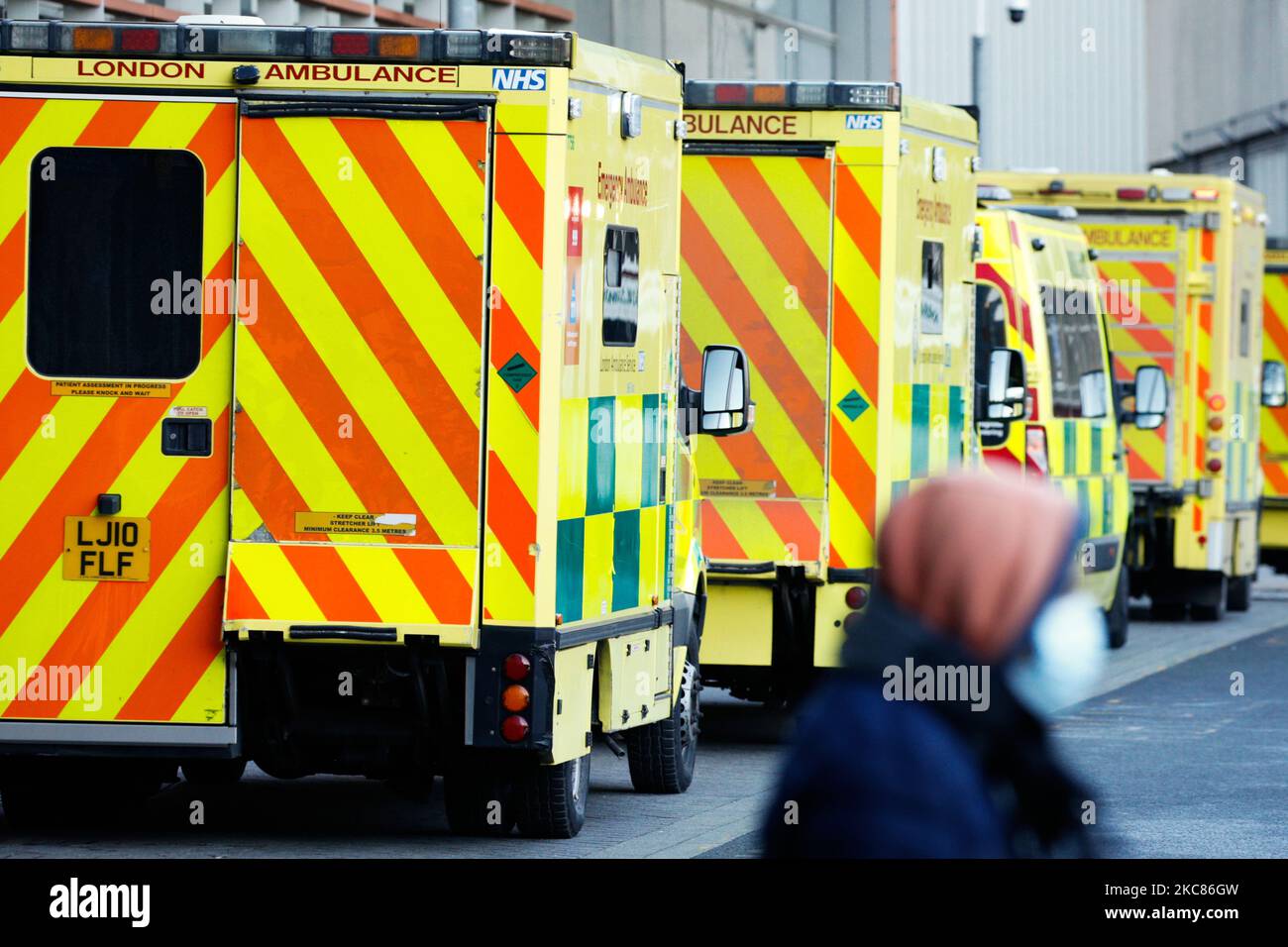 A member of the public wearing a face mask walks past ambulances