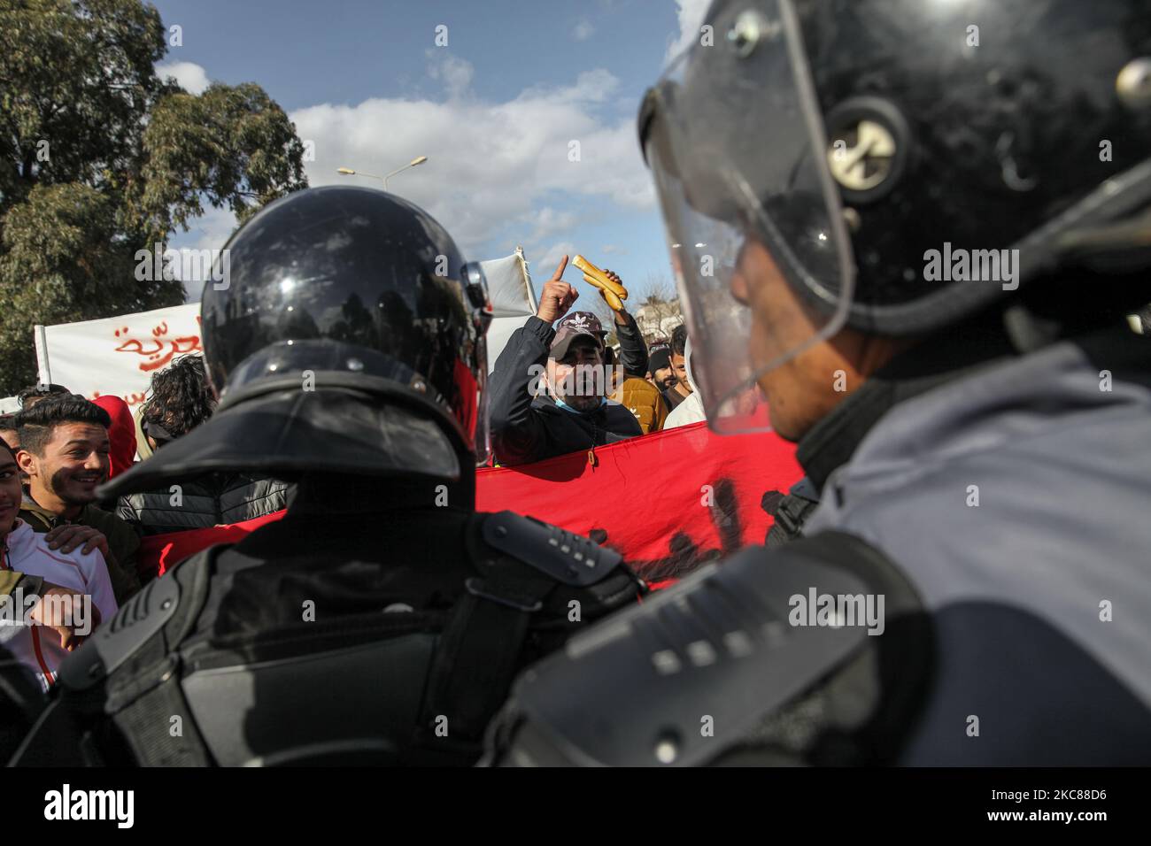 A protester raises a loaf of bread as another faces security forces members who prevent them from demonstrating in front of the building of the Assembly of the Representatives of the People (ARP) (Tunisian Parliament) in Bardo. Dozens of young people from the tough neighborhood of Hay Ettadhamen, which is one of the most populated cities in Tunis, took to the streets in an anti-government protest march that started from their neighborhood and headed towards Bardo city in Tunis. The demonstrators have particularly demanded the release of youths arrested by the police during the latest nightly p Stock Photo