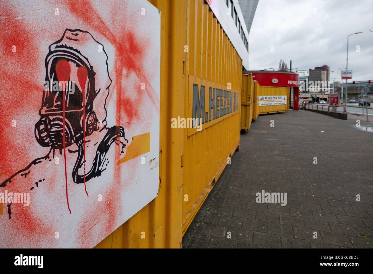 A sign of a man with chemical protection mask as seen vandalized with graffiti on the containers. The Philips Stadion, PSV club stadium in the Dutch city of Eindhoven is barricaded with shipping containers to protect the building, the museum, fanstore, multiple gates, trackside and supporters home side from riots and looting as happened previously in the city. The fortification and sealing of the front side of the stadium took place after the club received some threats according to the local media. Eindhoven faced some violent clashes during an anti-lockdown / anti-curfew protest that turned i Stock Photo