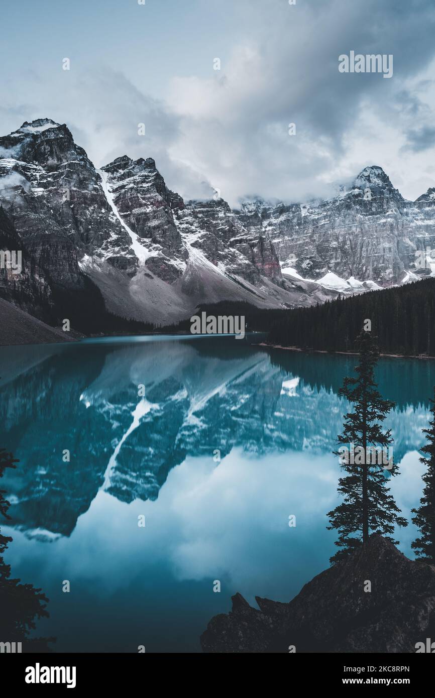 A long shot of lake moraine with surrounding trees and snow-capped mountains. Stock Photo