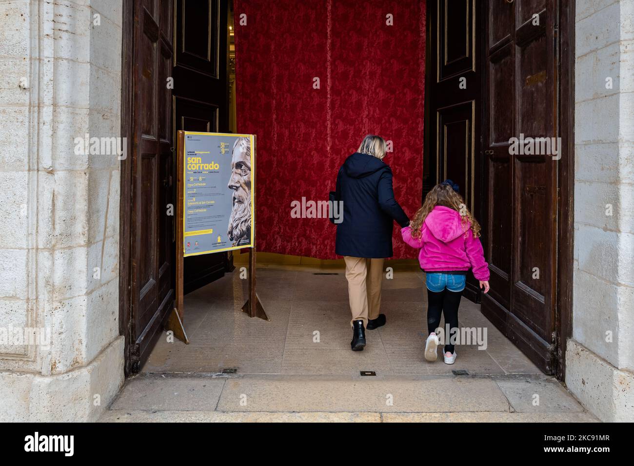 A lady and a child enter the Cathedral of Molfetta, before the start of the celebration of the Mass, on February 9, 2021 in Molfetta. February 9 is the liturgical feast dedicated to San Corrado, patron saint of Molfetta. On this date the Church remembers the day on which, according to tradition, the relics of the Saint were transferred from Modugno, the place of his death, to Molfetta. The feast of San Corrado this year, for obvious reasons related to the current health emergency, was devoid of celebrations that had seen the city community gather around the traditional lighting of bonfires but Stock Photo