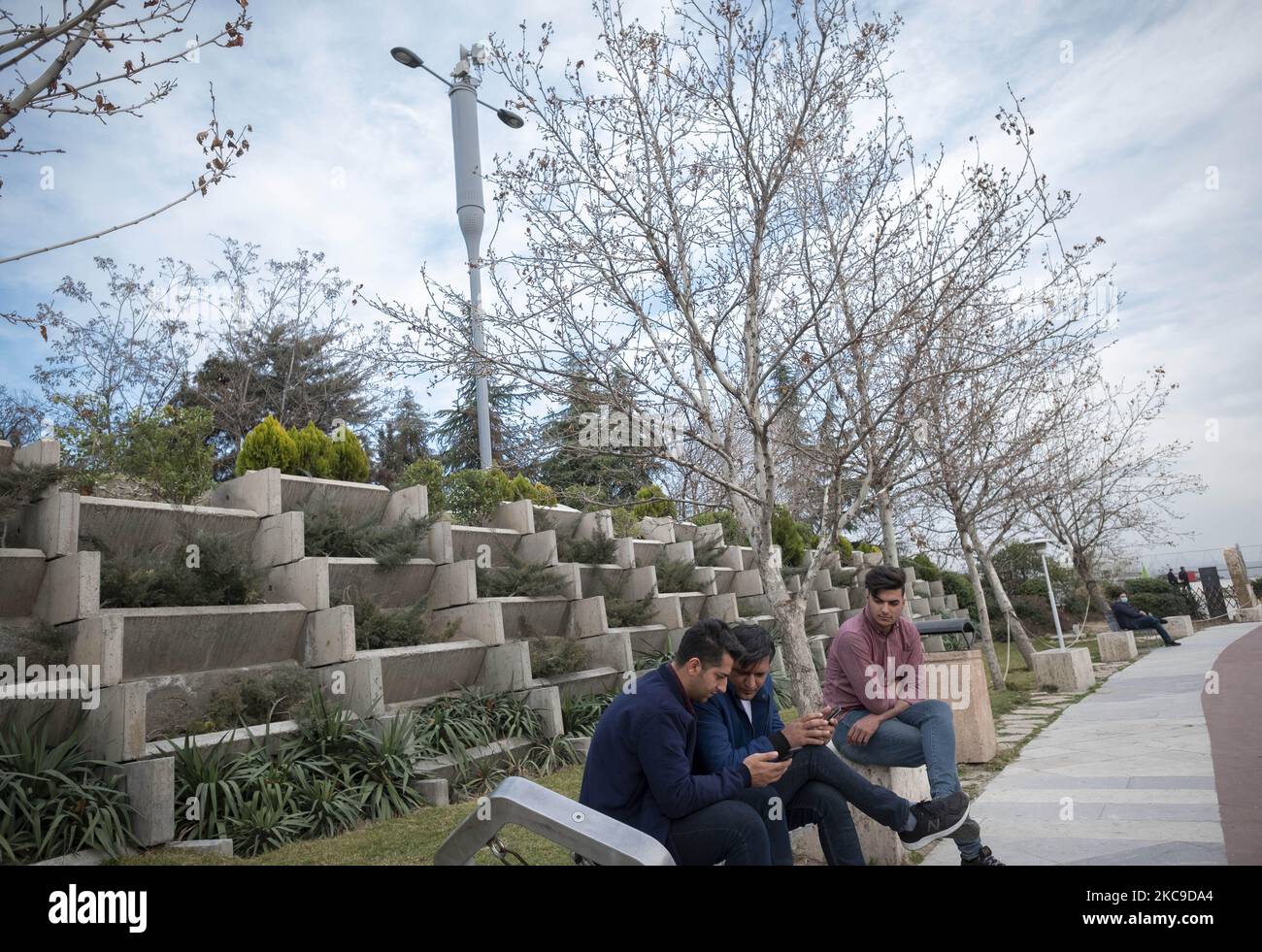 Iranian men use their smartphones as they sit under 5G