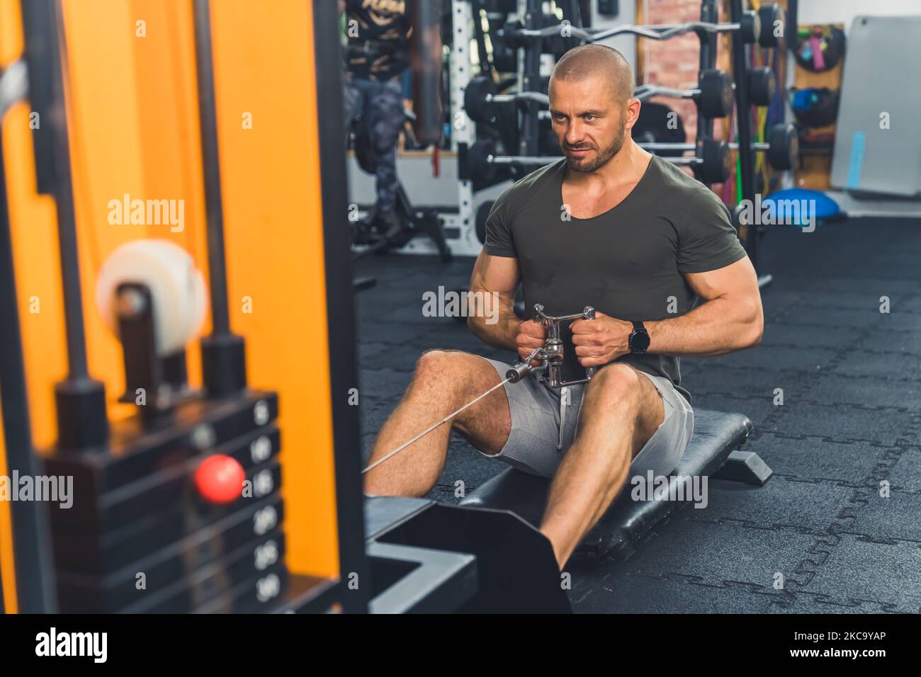 Full-length indoor shot of extremely focused caucasian muscular bald male bodybuilder exercising at gym in dark t-shirt and gray shorts. High quality photo Stock Photo