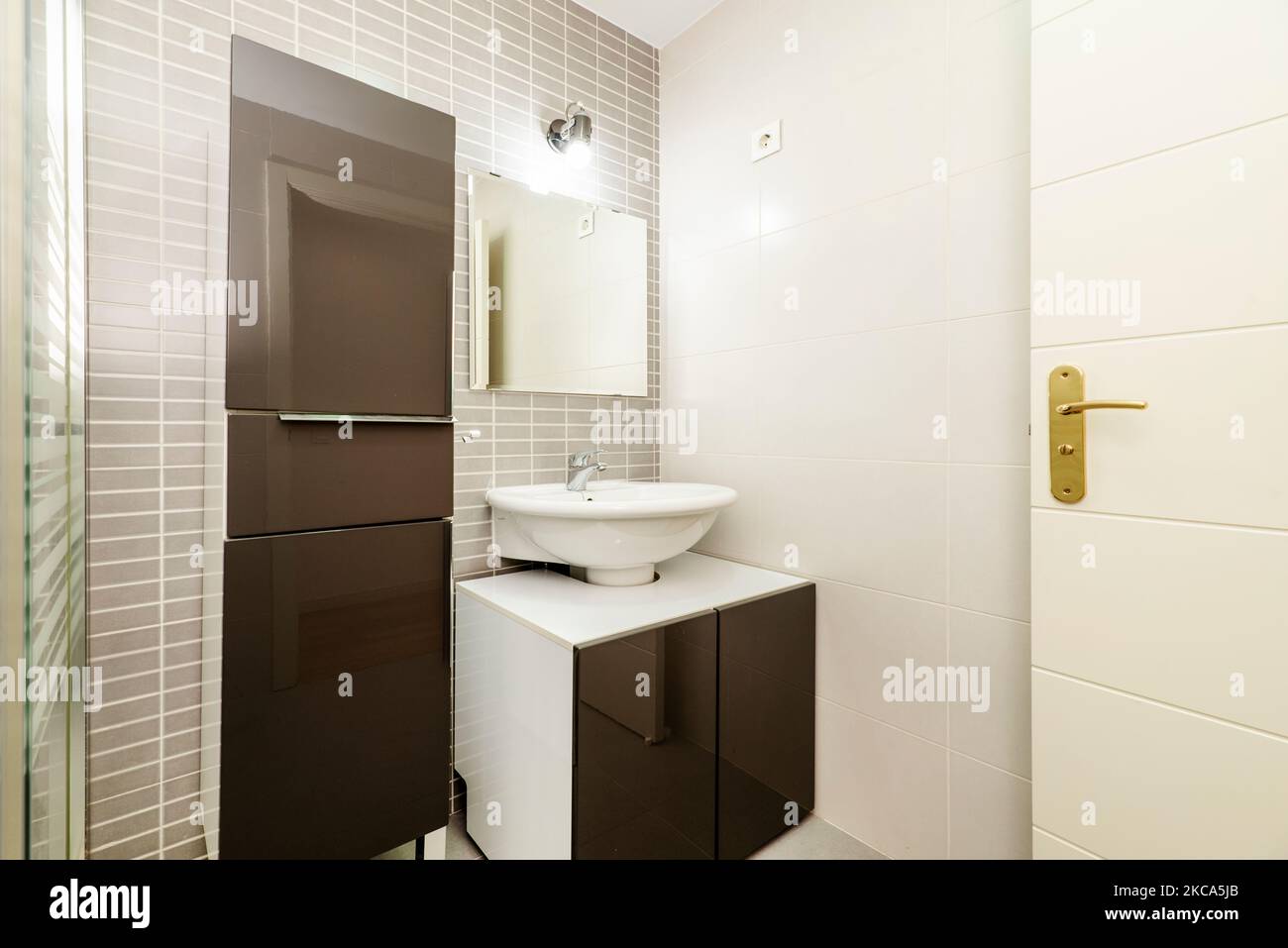 Toilet with small white chest of drawers with brown doors with frameless square mirror and matching column cabinet Stock Photo