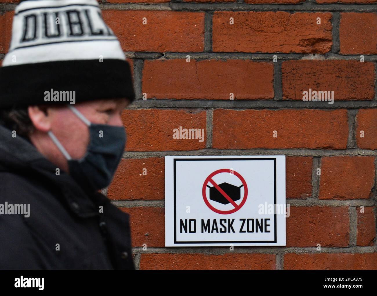 A man wearing a face mask walks by a sign 'No Mask Zone' outside Hemp Land shop in Dublin during Level 5 Covid-19 lockdown. On Tuesday, March 2, 2021, in Dublin, Ireland. (Photo by Artur Widak/NurPhoto) Stock Photo