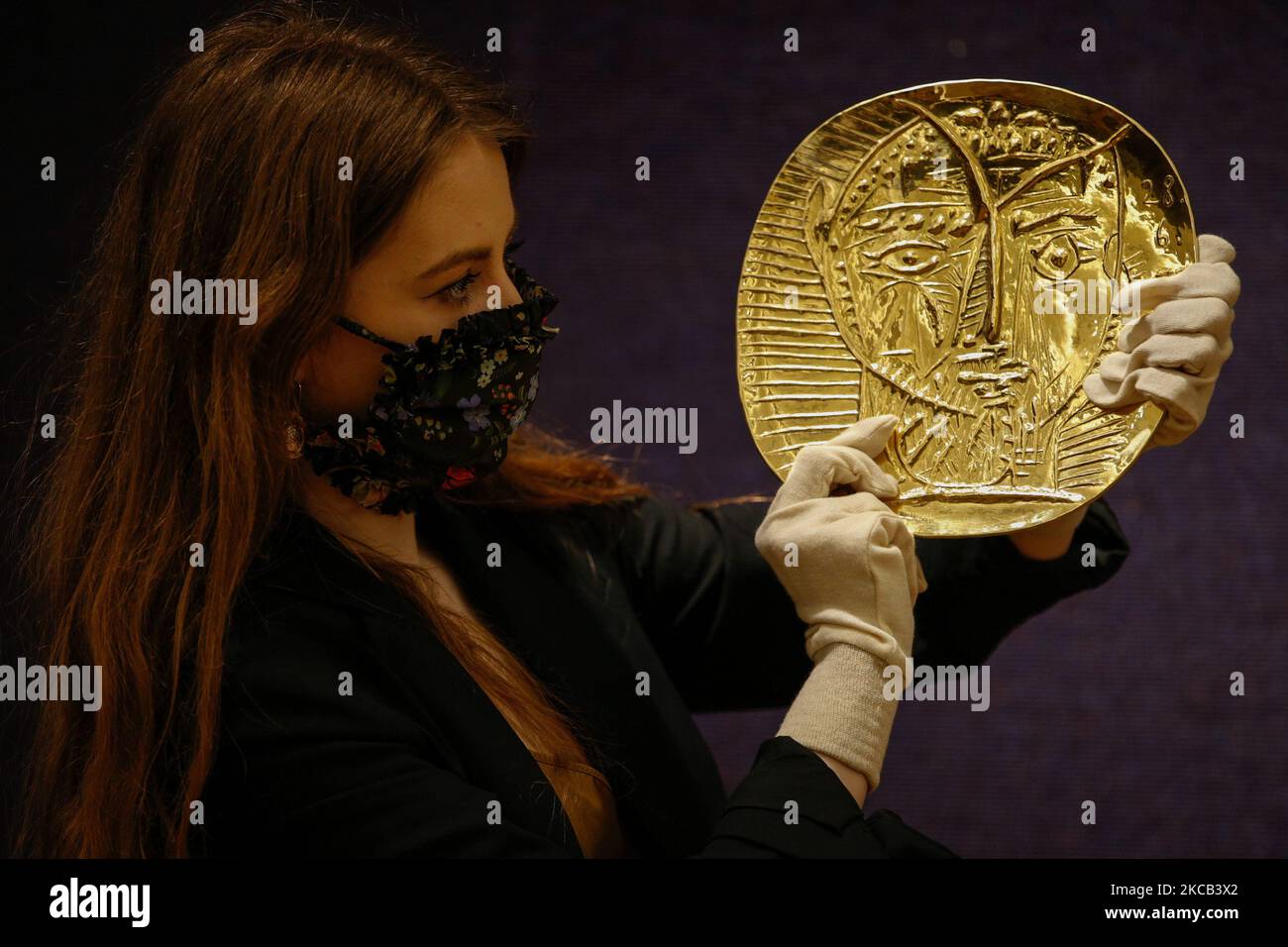 A member of staff poses with gold plate 'Visage de faune', by Spanish artist Pablo Picasso, estimated at GBP250,000-350,000, during a press preview for the upcoming 'Picassomania' sale at Bonhams auction house in London, England, on March 18, 2021. The sale takes place next Tuesday, March 23. (Photo by David Cliff/NurPhoto) Stock Photo