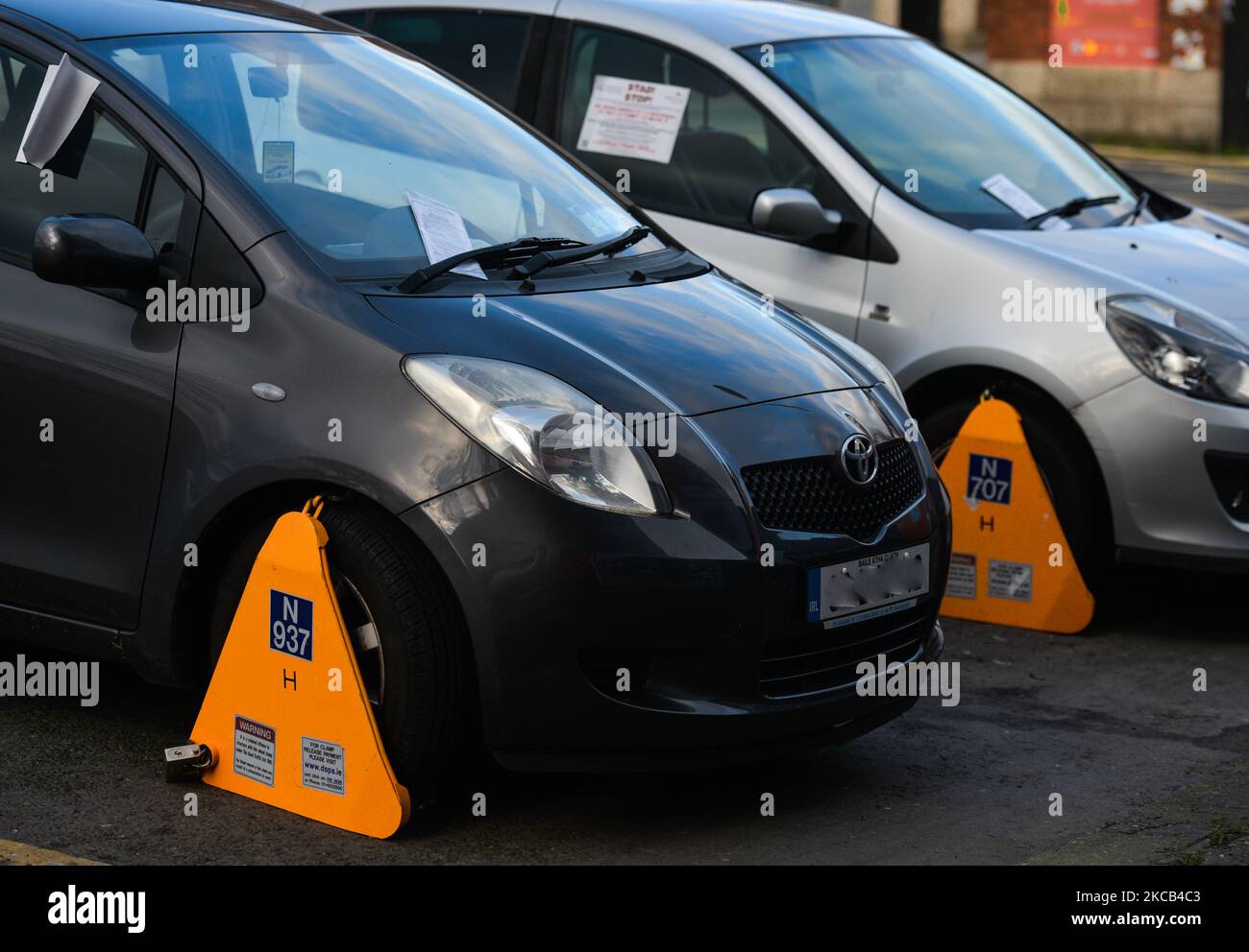Two cars locked with a yellow clamped wheel lock by traffic authorities