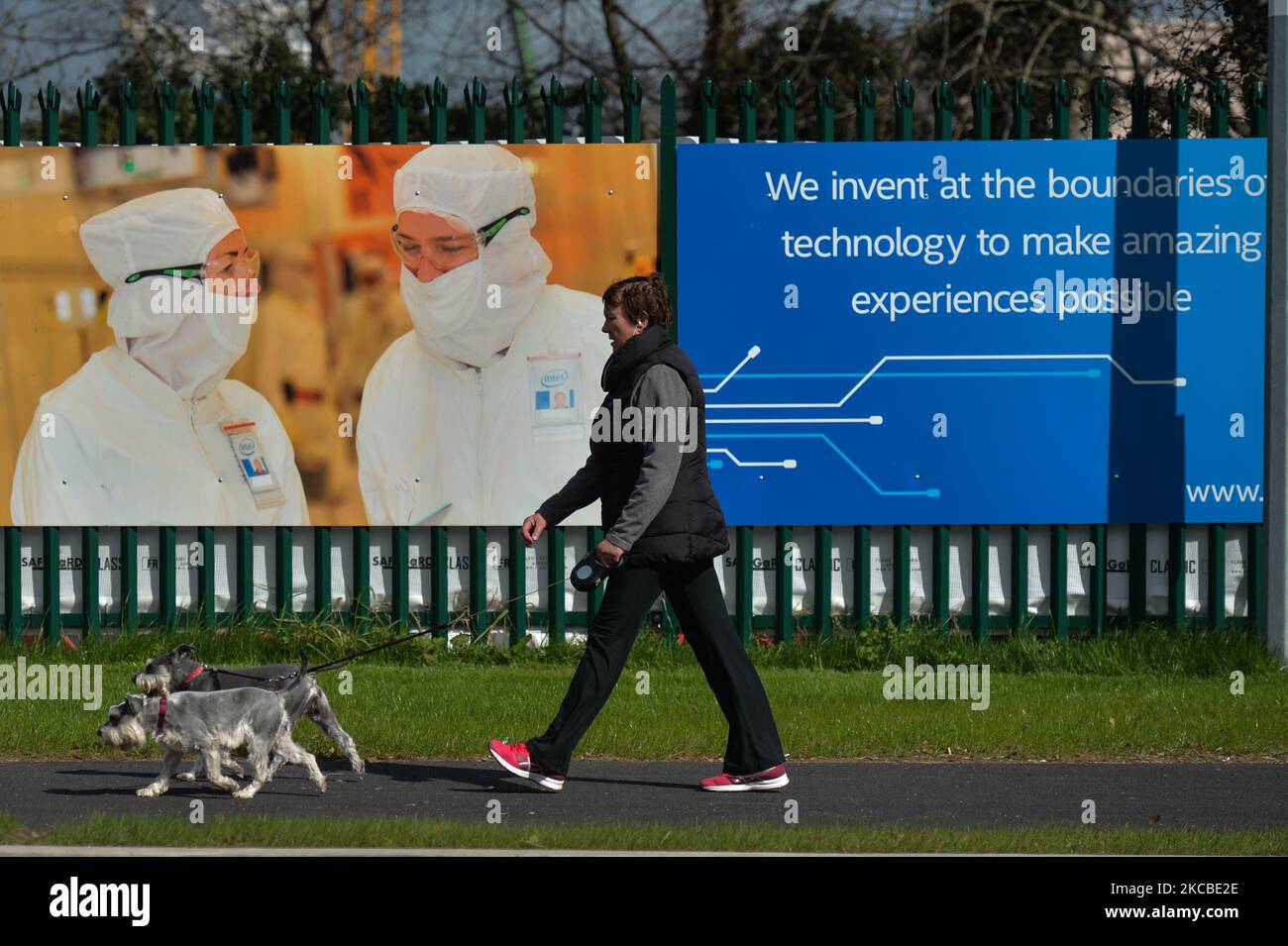 A woman walks dogs by the construction site fence of a new microchip manufacturing facility on Intel's Leixlip campus in Co. Kildare after the company announced the creation of 1,600 new jobs at the facility. On Wednesday, March 23, 2021, in Leixlip, County Kildare, Ireland. (Photo by Artur Widak/NurPhoto) Stock Photo