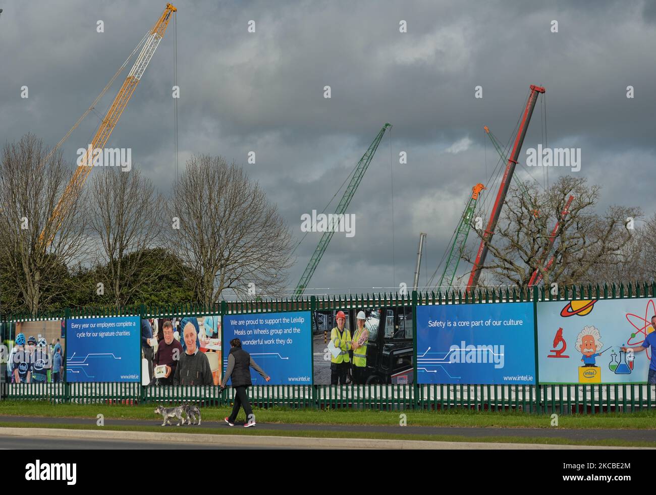 A woman walks dogs by the construction site fence of a new microchip