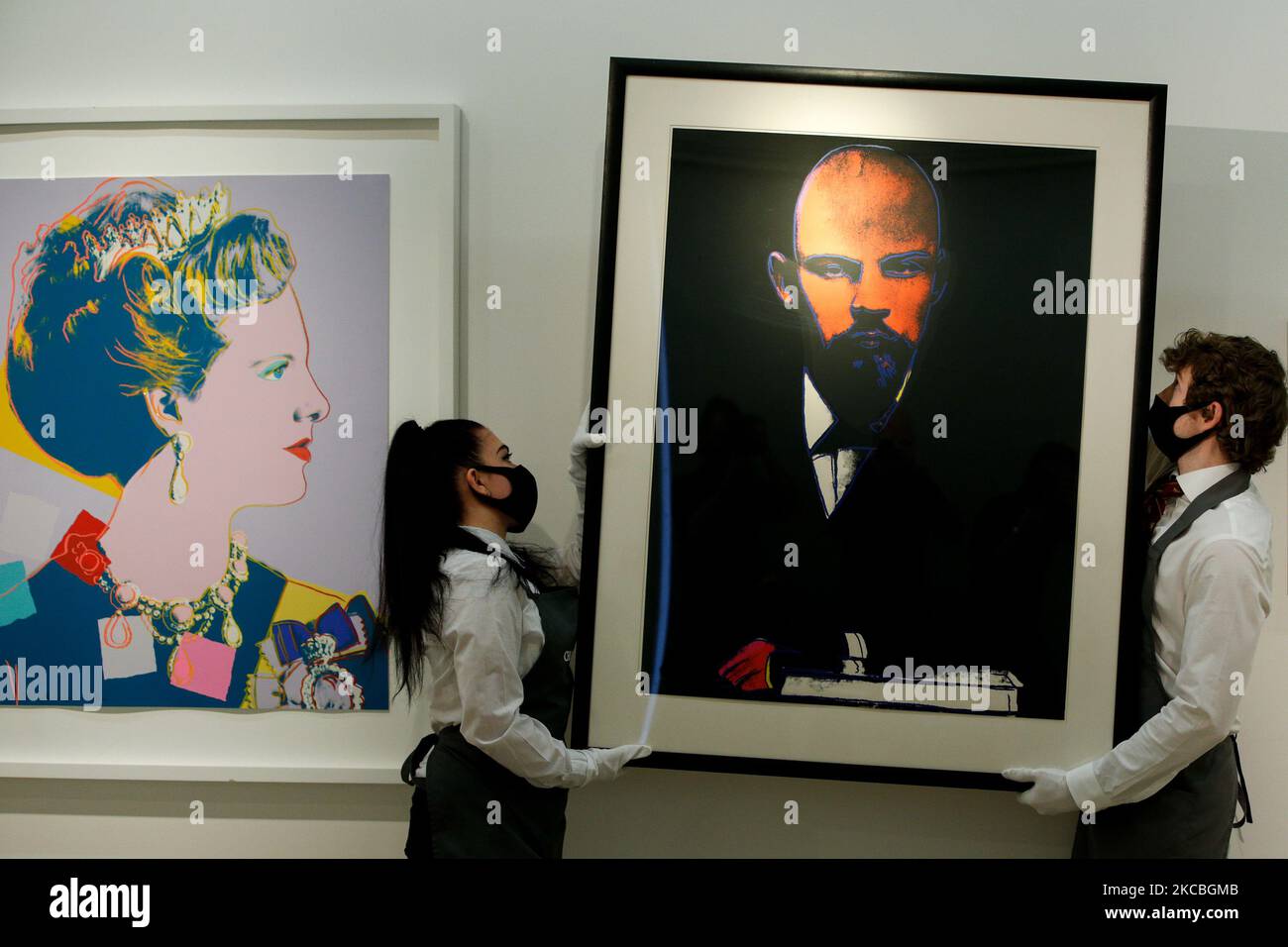 Art handlers poses holding 'Lenin', by American artist Andy Warhol, estimated at GBP50,000-70,000, and beside one of Warhol's set of four 'Queen Margarethe II of Denmark, from: Reigning Queens (Royal Edition)', estimated at GBP60,000-80,000, during a press preview at Christie's auction house in London, England, on March 26, 2021. (Photo by David Cliff/NurPhoto) Stock Photo