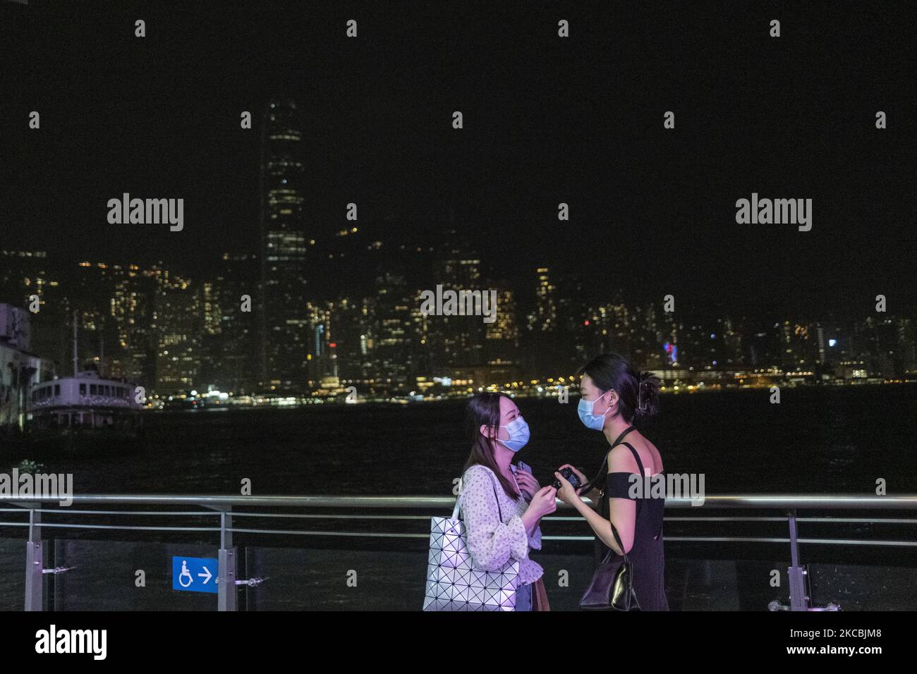 Two women are seen talking while standing in front of the Hong Kong Skyline with lights turned off in Hong Kong, Saturday, 27 March, 2021. Today some buildings in Hong Kong will close their lights for an hour for the Earth Hour environmental campaign. (Photo by Vernon Yuen/NurPhoto) Stock Photo