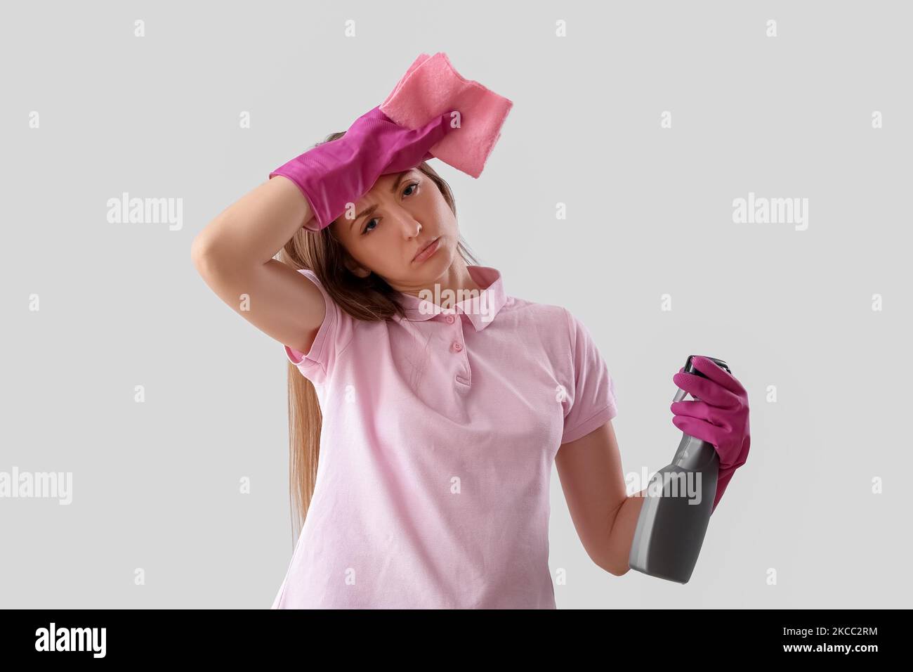 Tired young woman with spray bottle of detergent and rag on light ...