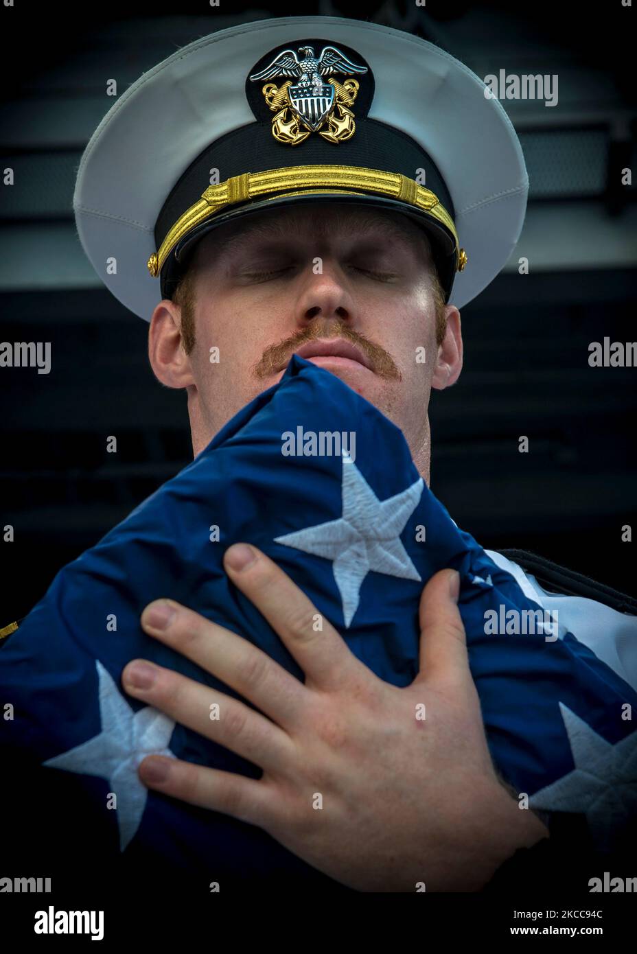 U.S. Navy sailor holds the national ensign and bows his head in prayer. Stock Photo