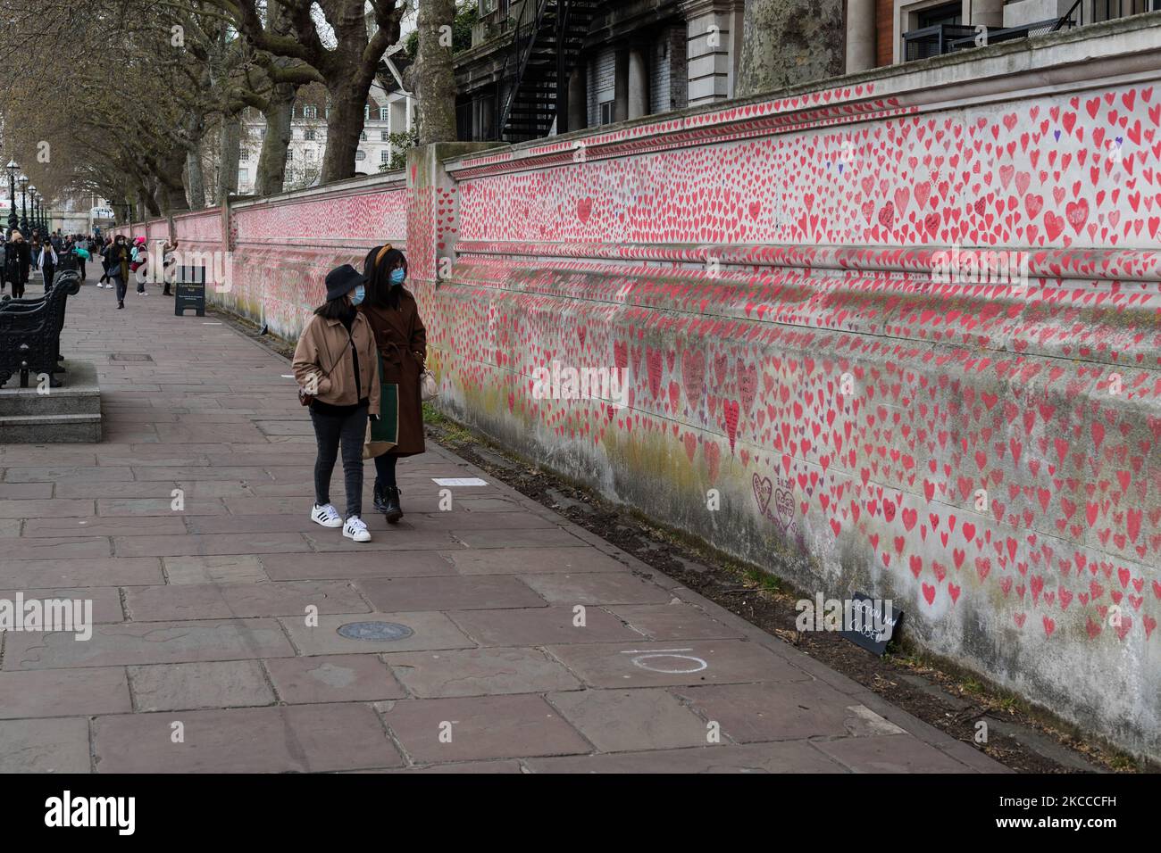 LONDON, UNITED KINGDOM - APRIL 07, 2021: People walk past a memorial for the victims of Covid-19 outside St Thomas’ Hospital on 07 April, 2021 in London, England. The mural, set up by Covid-19 Bereaved Families for Justice on Monday last week, has so far seen around 130,000 hand-drawn hearts placed on a kilometre-long section of wall facing the Houses of Parliament. (Photo by WIktor Szymanowicz/NurPhoto) Stock Photo