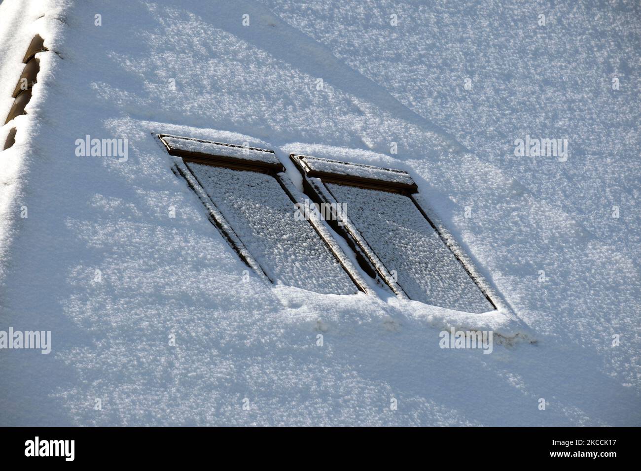 Closeup of house roof top with attic windows covered with snow in cold