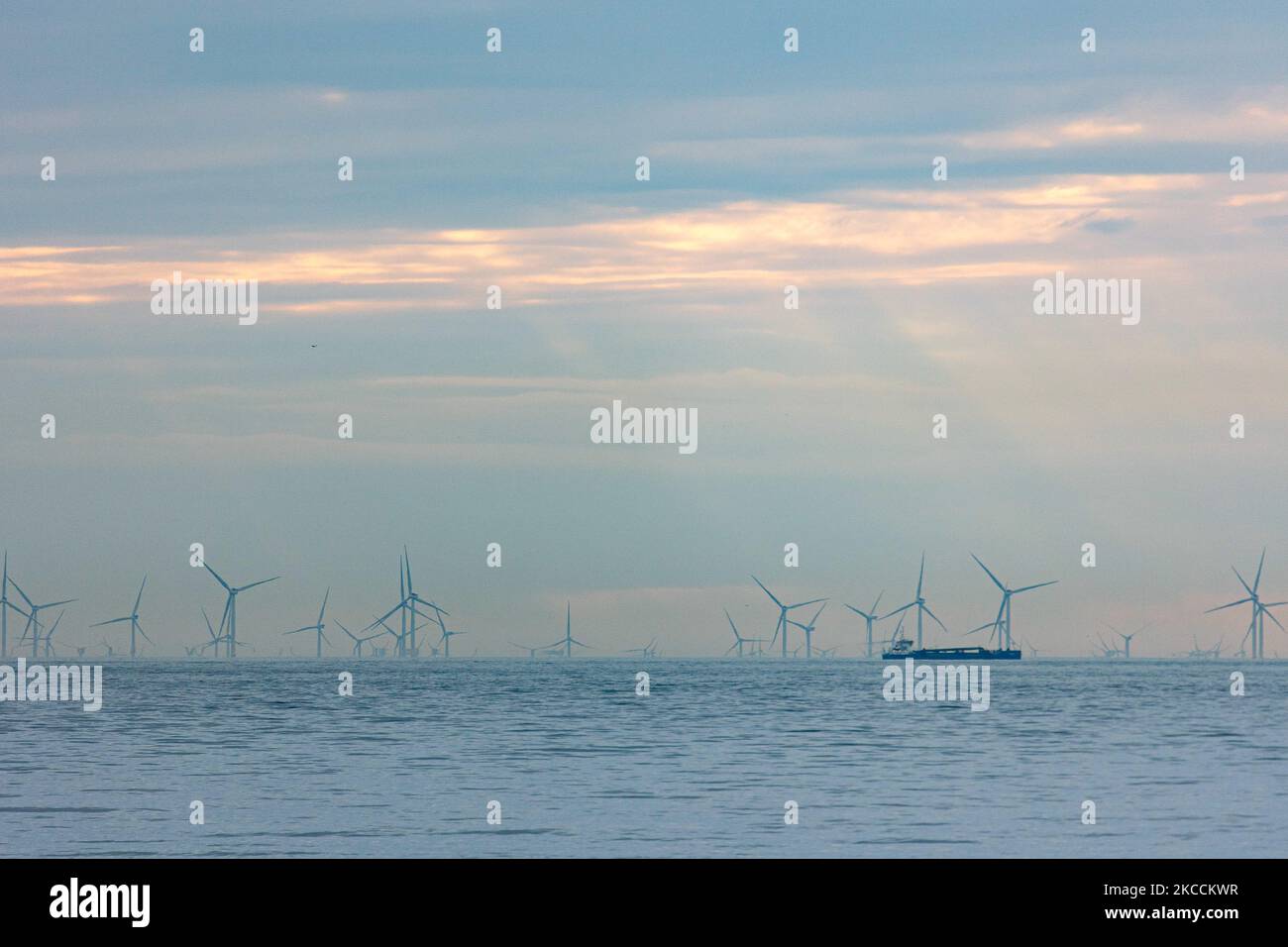 Off-shore wind park of windmills generating green renewable electric energy 20 kilometers away from the Dutch coast between the Netherlands and the United Kingdom during dusk sunset time, with clouds and ships over the horizon of the sea. The wind turbine generators create sustainable green energy from the wind power, jet stream of air in the atmosphere, the park installed in the North Sea as seen from Oosterschelde in Zeeland in the Netherlands on April 10, 2021 (Photo by Nicolas Economou/NurPhoto) Stock Photo