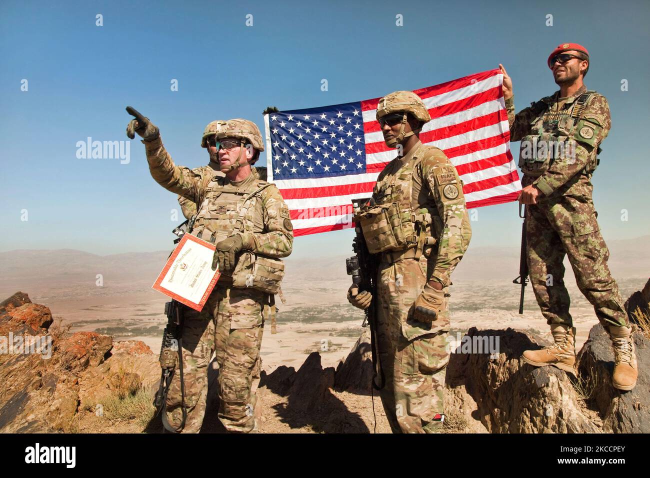 U.S. Army soldiers hold the American flag atop Pride Rock mountain in Afghantistan. Stock Photo