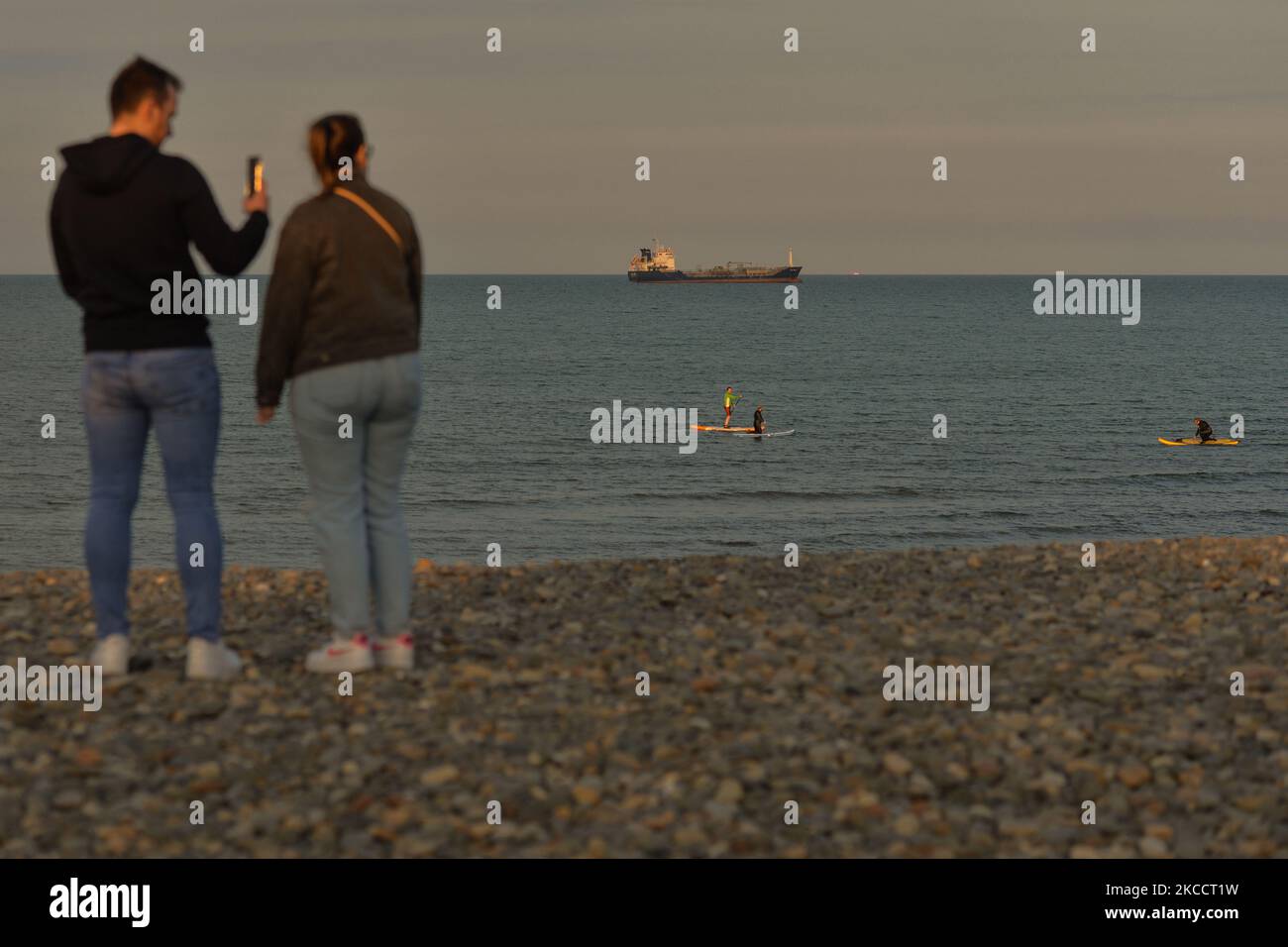 A couple watch the paddleboarders training near Bray's rocky beach, during the COVID-19 lockdown. On Thursday, 15 April 2021, in Bray, County Wicklow, Ireland. (Photo by Artur Widak/NurPhoto) Stock Photo