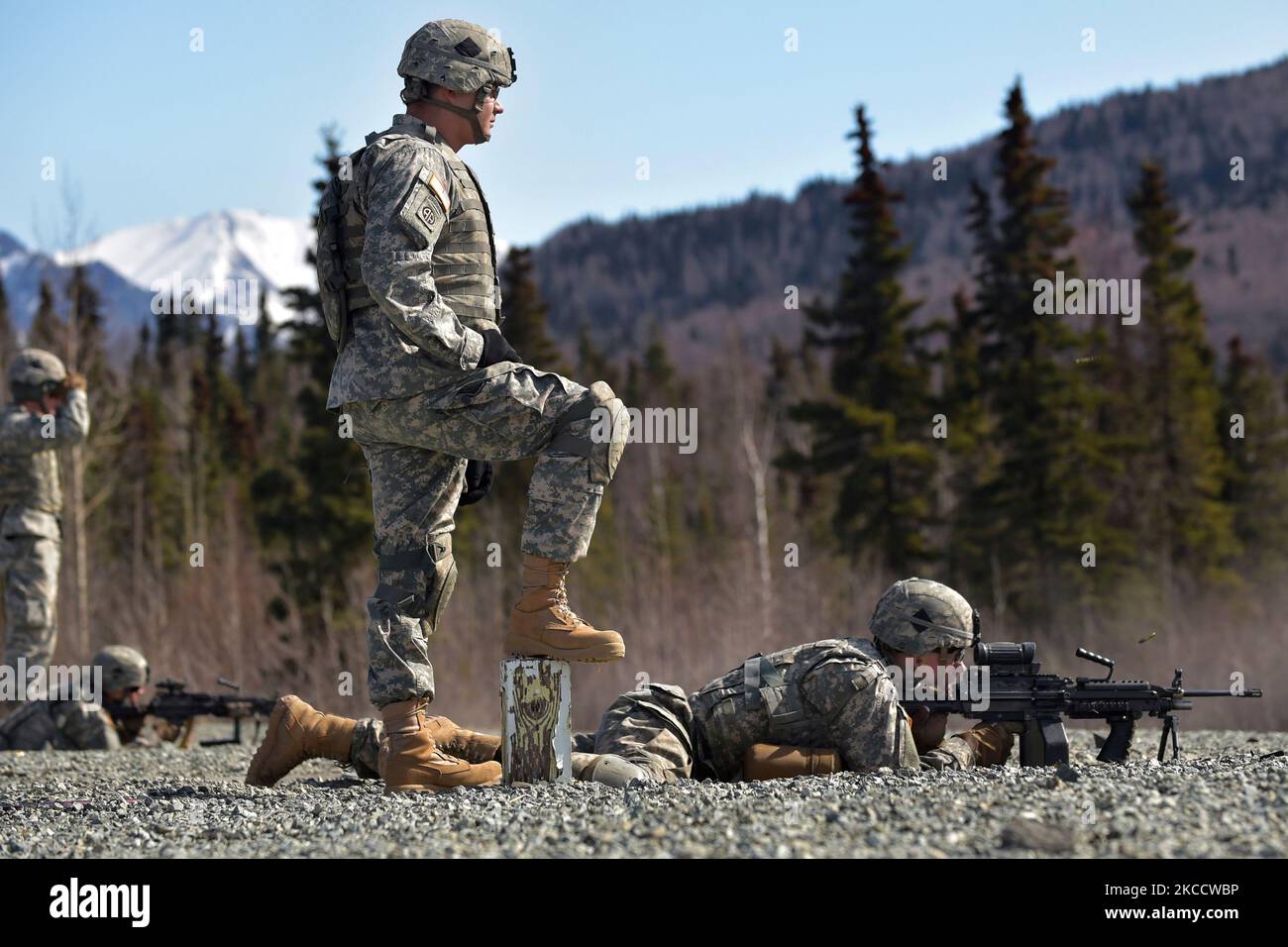 U.S. Army Soldier watches a fellow soldier fire an M249 Squad Automatic Weapon. Stock Photo