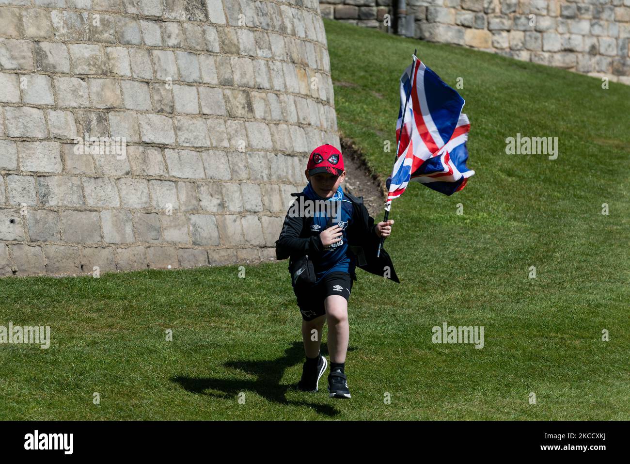 A child runs outside Windsor Castle holding a Union Jack flag ahead of the funeral of Britain's Prince Philip in Windsor, Britain, 17 April 2021. The Duke of York. Prince Philip, the Consort of the longest reigning English monarch in history, Queen Elizabeth II, died on 9 April 2021, two months before his 100th birthday. (Photo by Maciek Musialek/NurPhoto) Stock Photo
