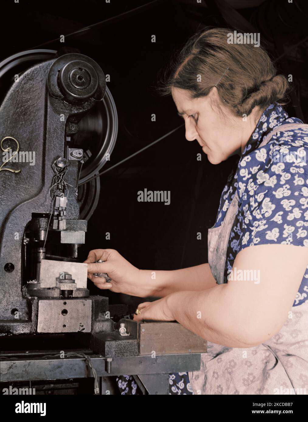 Woman worker punching holes in electrical terminals with a power press, 1942. Stock Photo