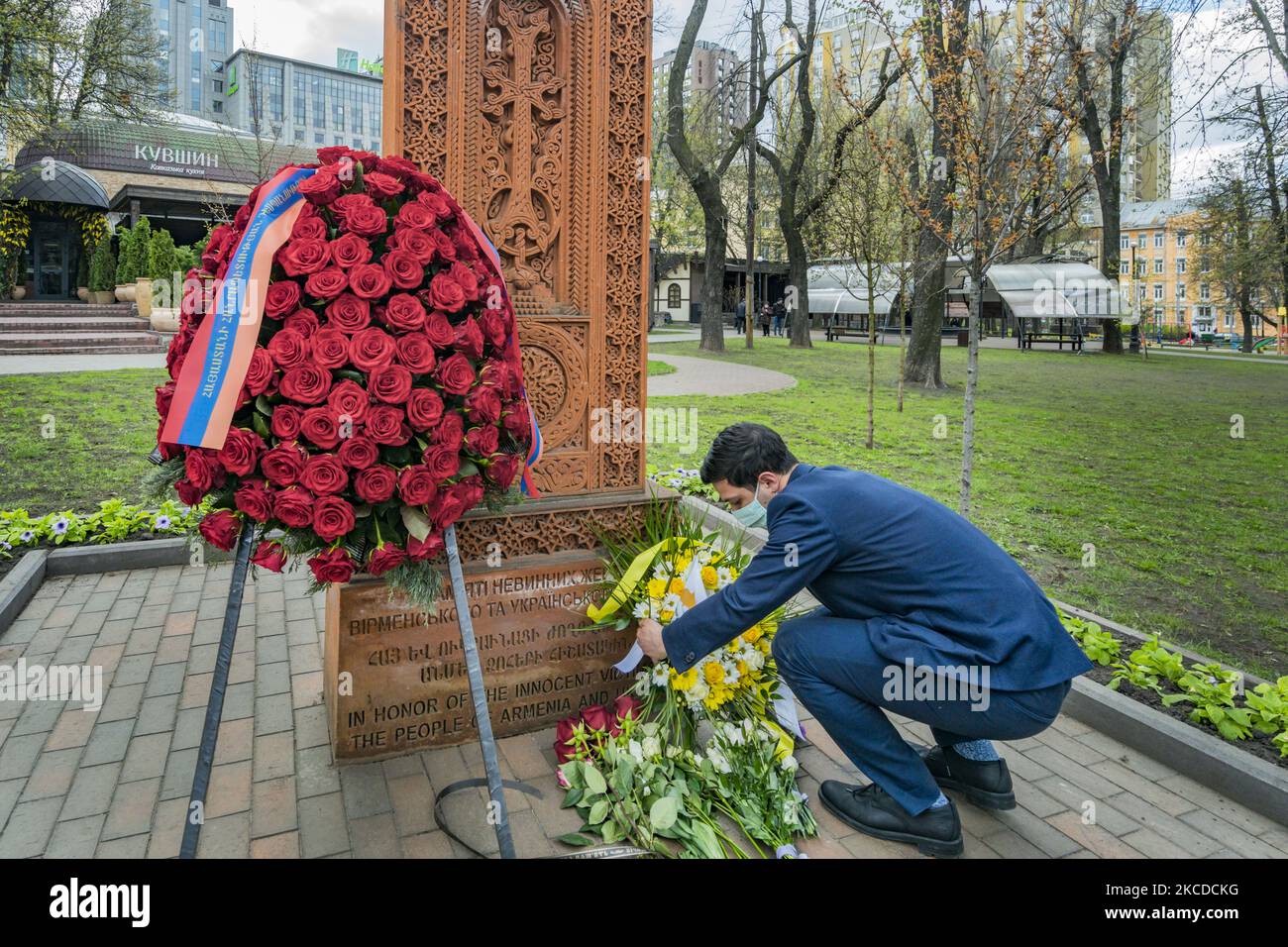 A man leaves a flower offering under a khachkar, a memorial stone stele