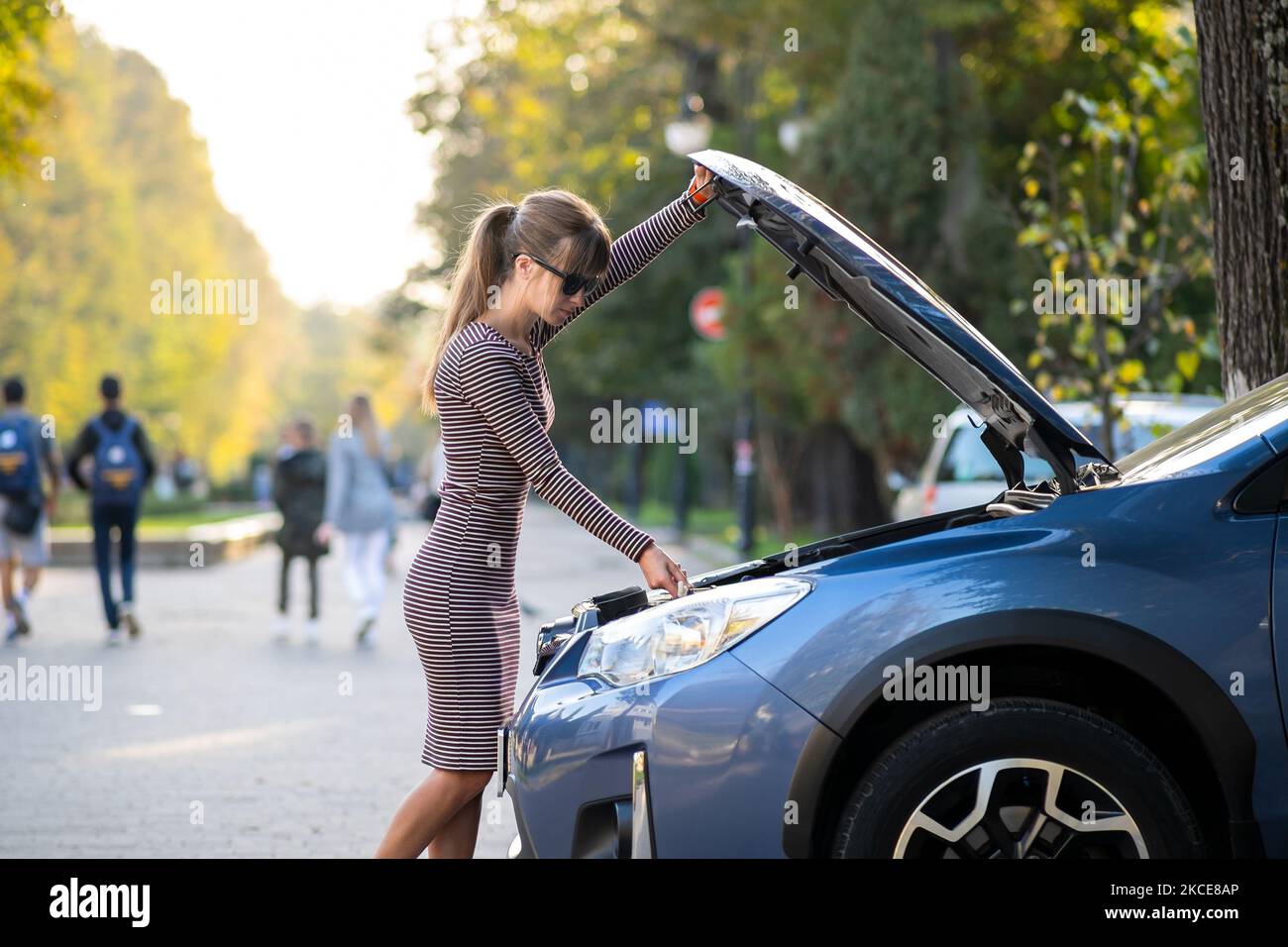 Female driver opening car hood inspecting broken engine on a city