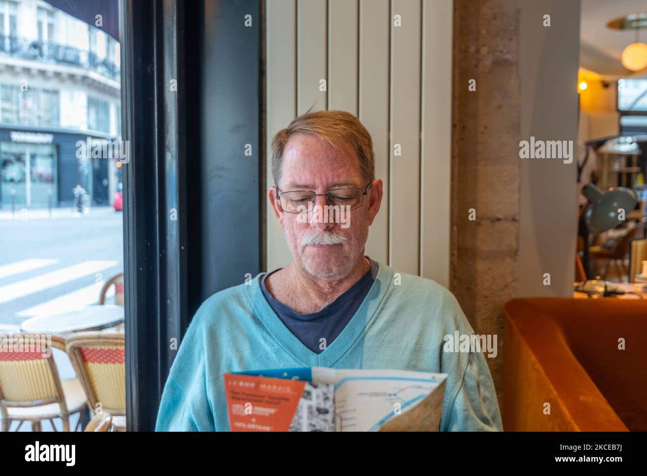 Senior with map and city guide of Paris, sitting in cafe.  Stock Photo